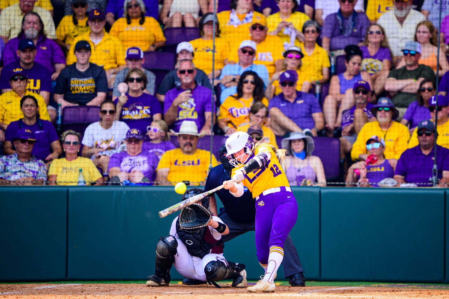 LSU softball player at bat during game with purple and gold crowd in background.