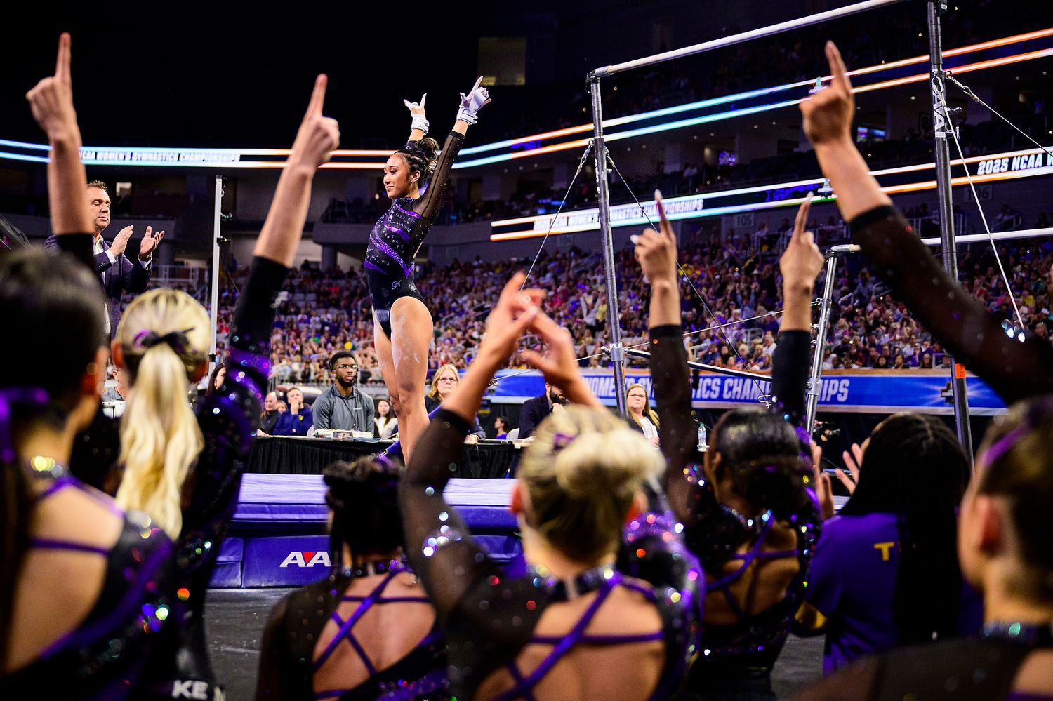 Cheerleaders in purple uniforms celebrate with raised arms during a sports event performance at an indoor arena.