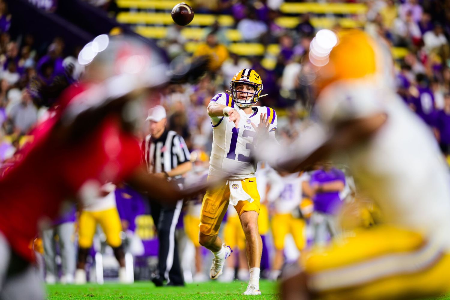 LSU quarterback throws a pass during a football game while opposing players rush towards him.