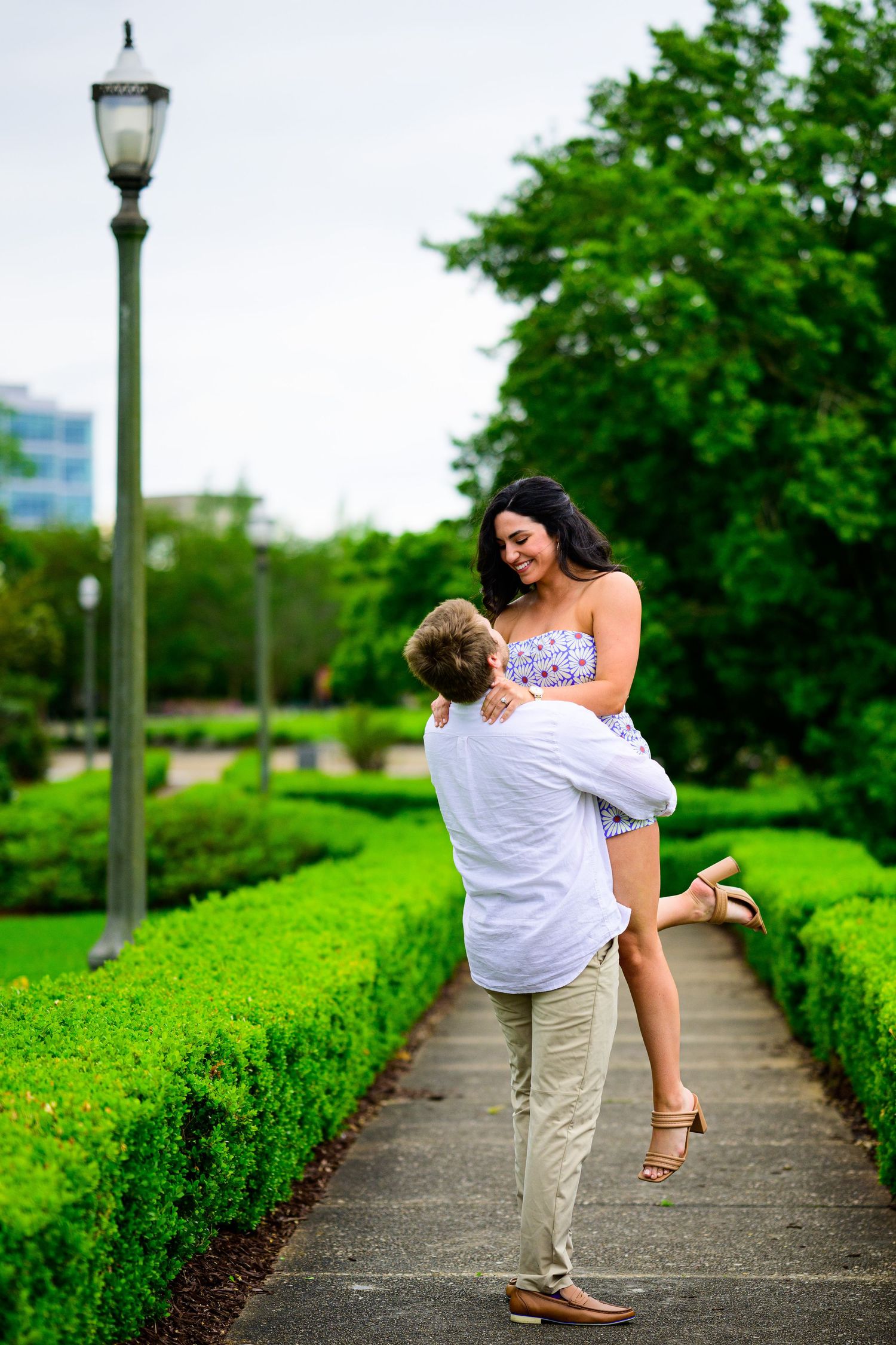 Romantic couple embraces on a garden path surrounded by manicured hedges and a vintage lamp post.