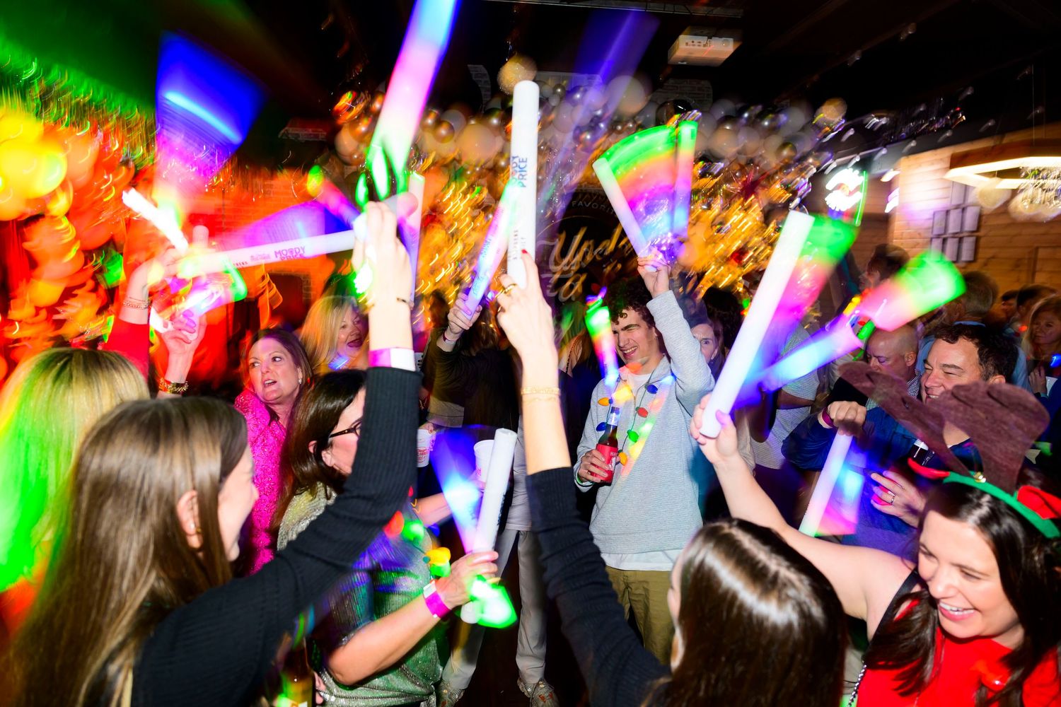 Crowd waves colorful glow sticks in dark nightclub with vibrant lighting effects.