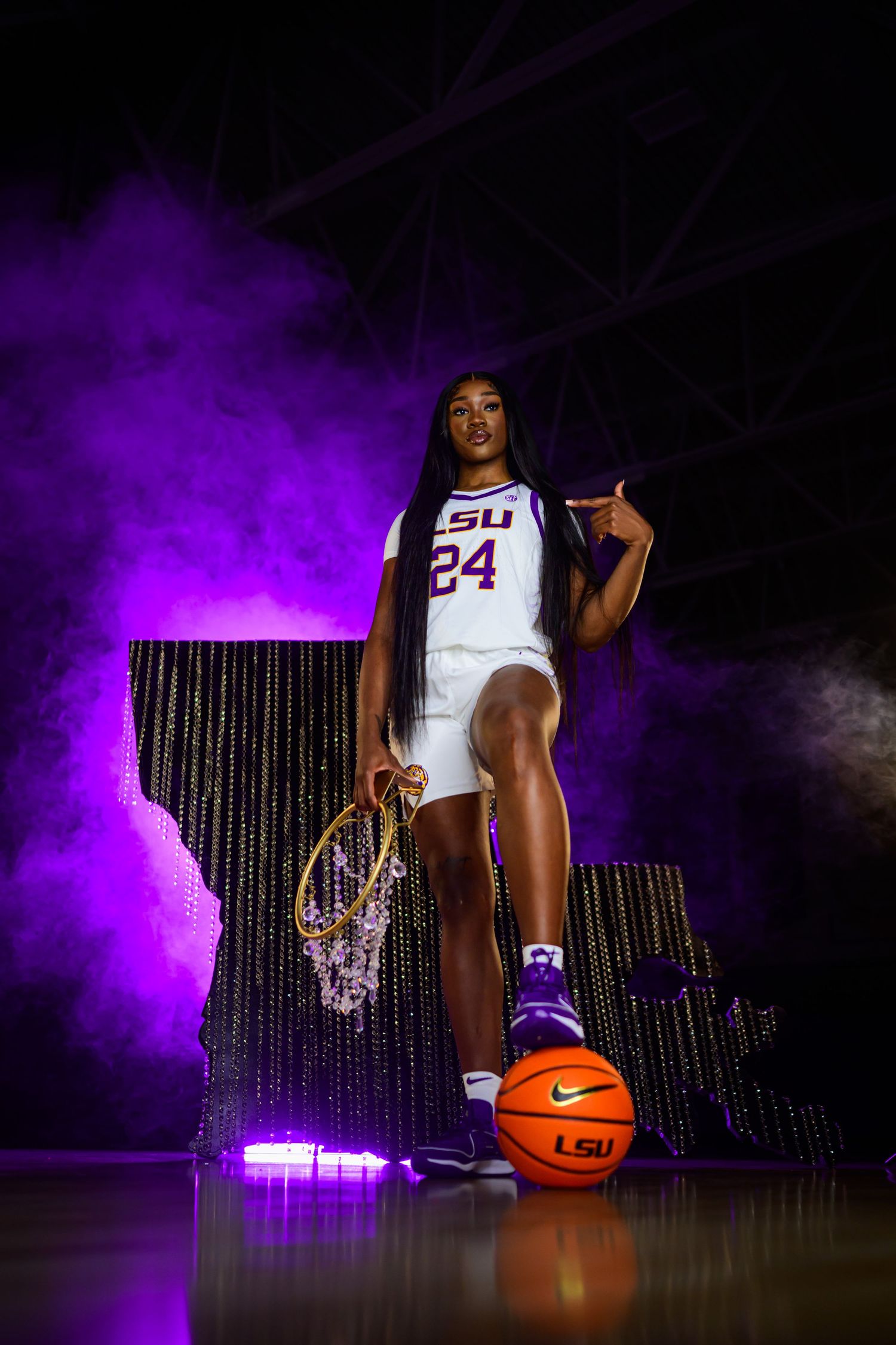 Basketball player poses in LSU uniform number 34 with dramatic purple lighting and smoke effects on dark background.