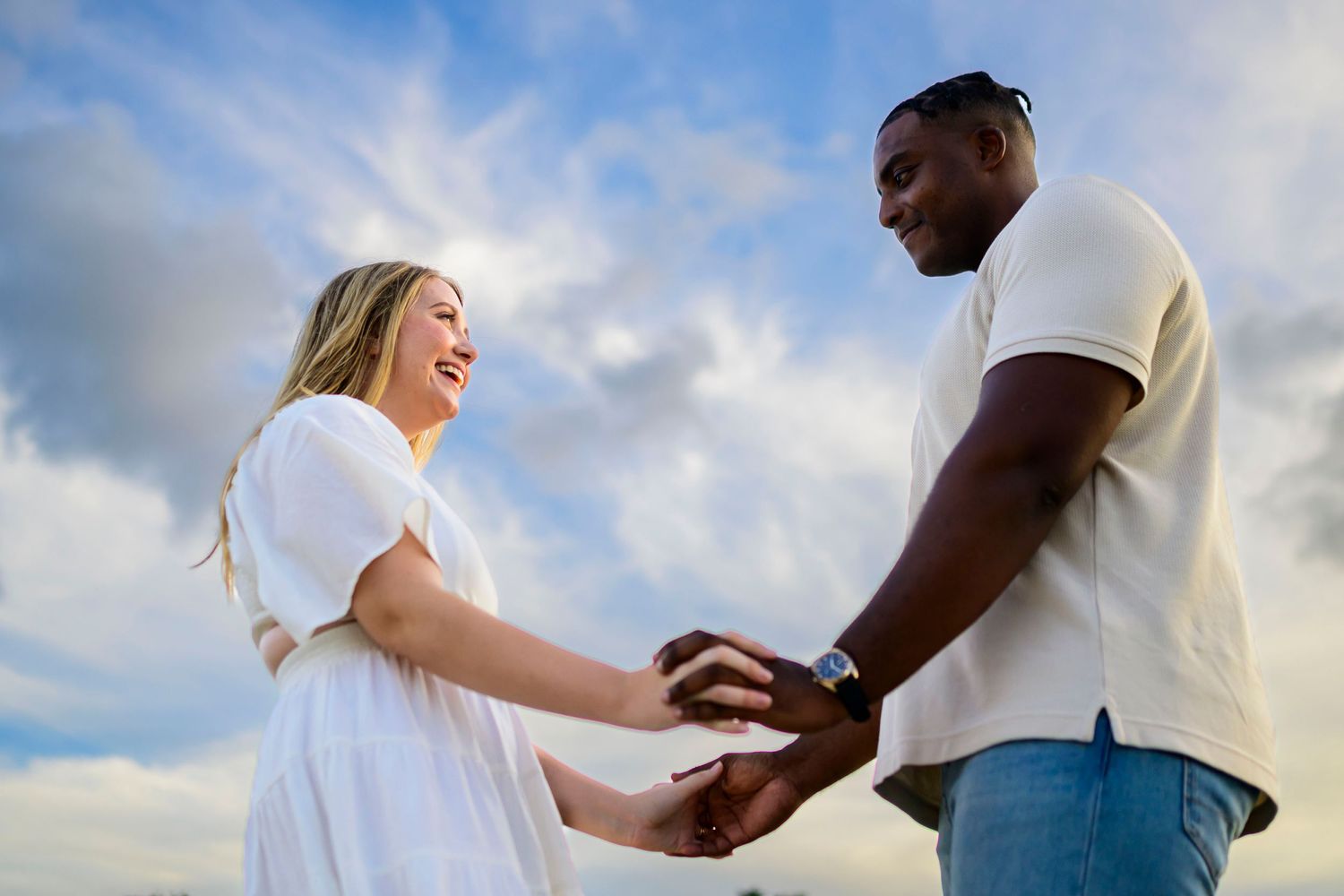 Couple sharing a joyful moment against dramatic cloudy sky at sunset.