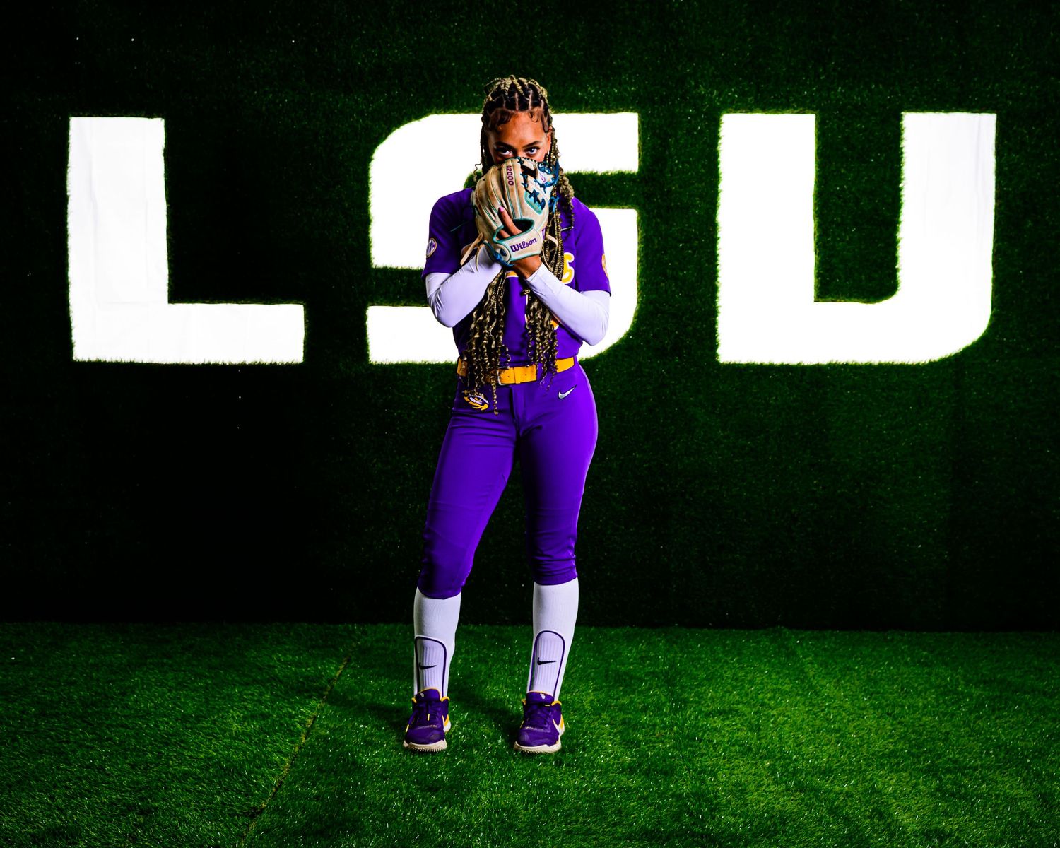 Athlete posing in purple uniform in front of illuminated LSU text display.