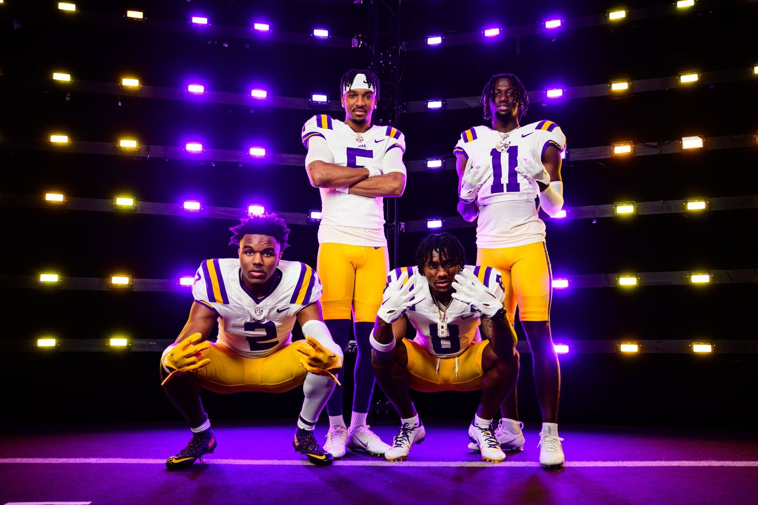 LSU football players pose in the team's signature purple and gold uniforms on an illuminated stage during media day.
