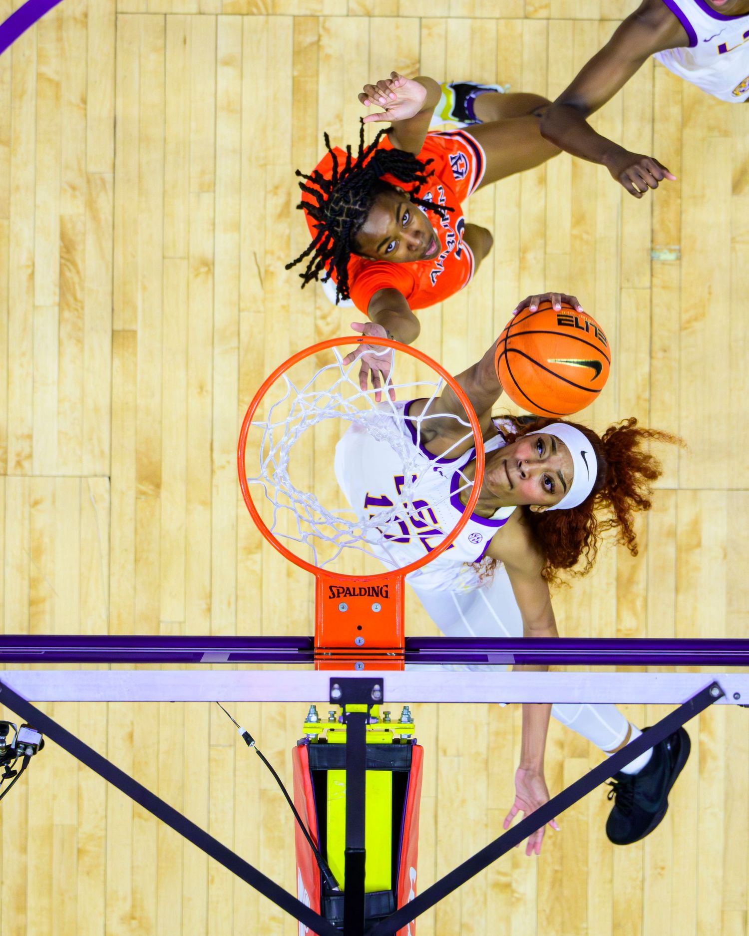Aerial view of basketball players competing for a rebound near the hoop on a wooden court during a game.