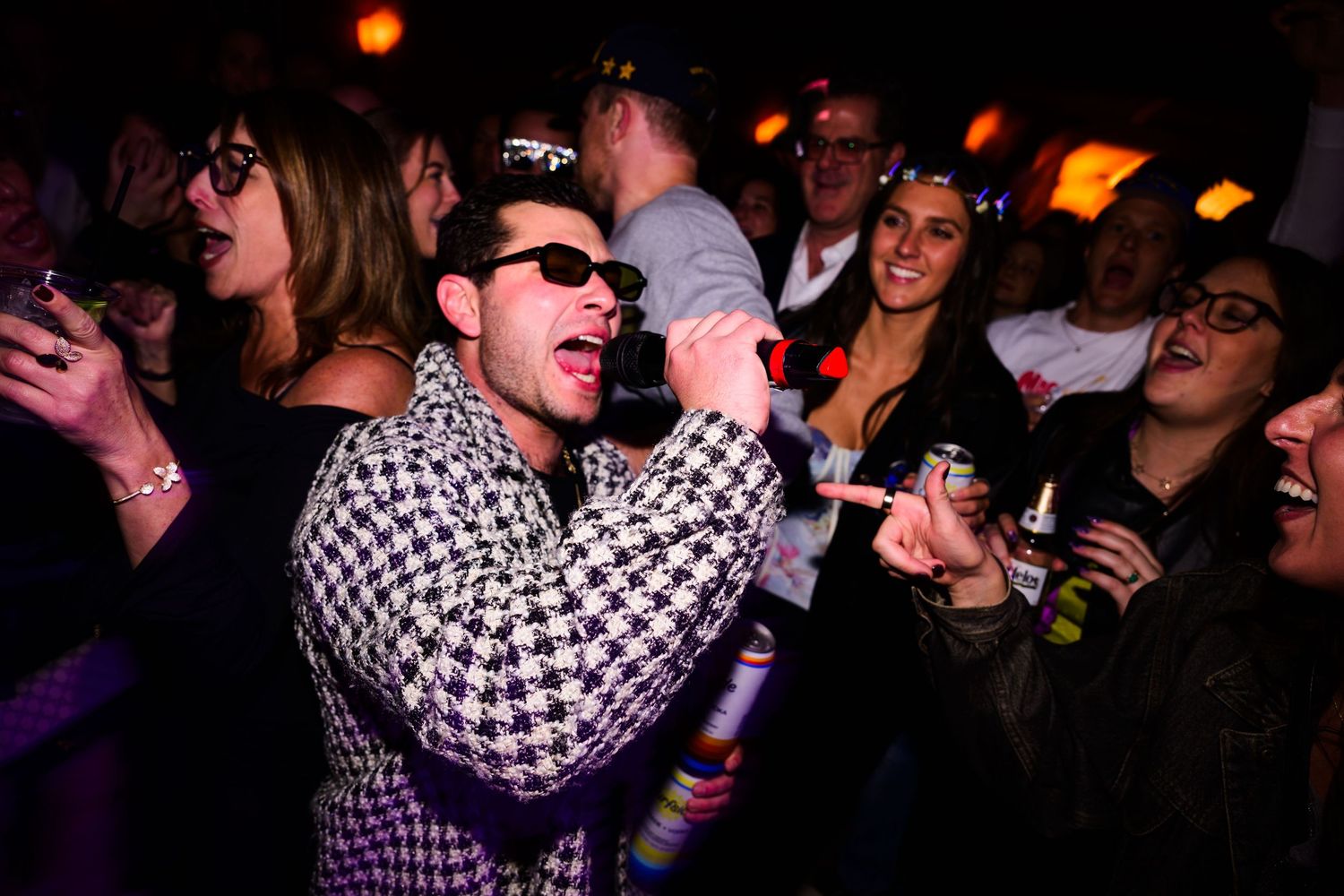 Performer in a checkered shirt sings passionately on stage at a crowded concert venue.
