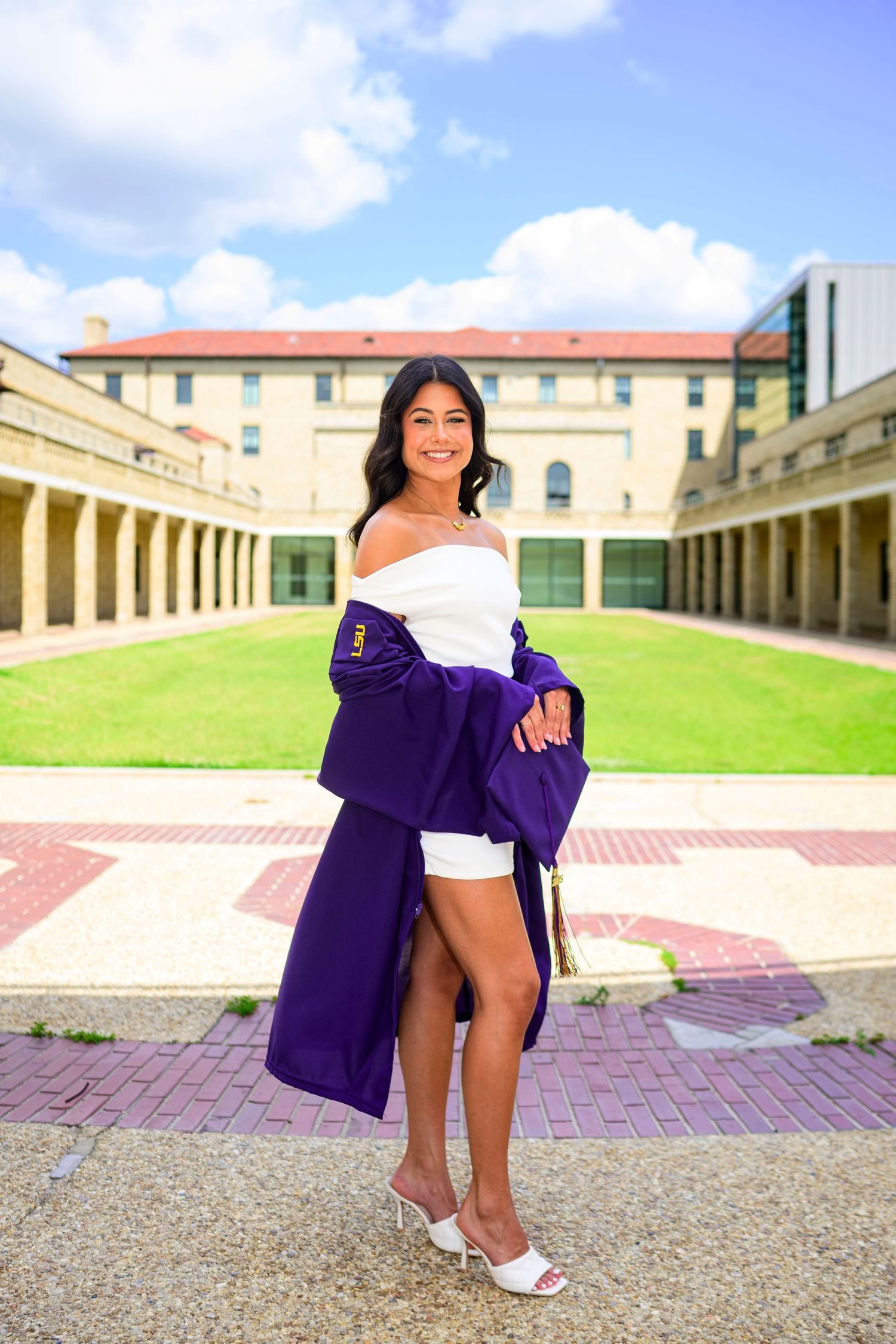 Graduate in purple graduation gown poses in historic LSU quadrangle courtyard.