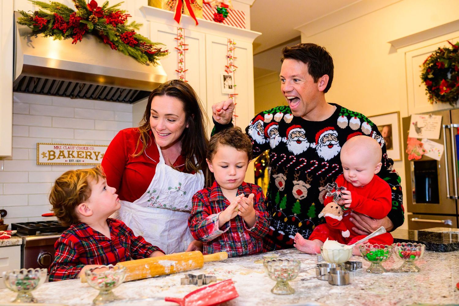 Family baking together in kitchen decorated with holiday garland and festive decorations.