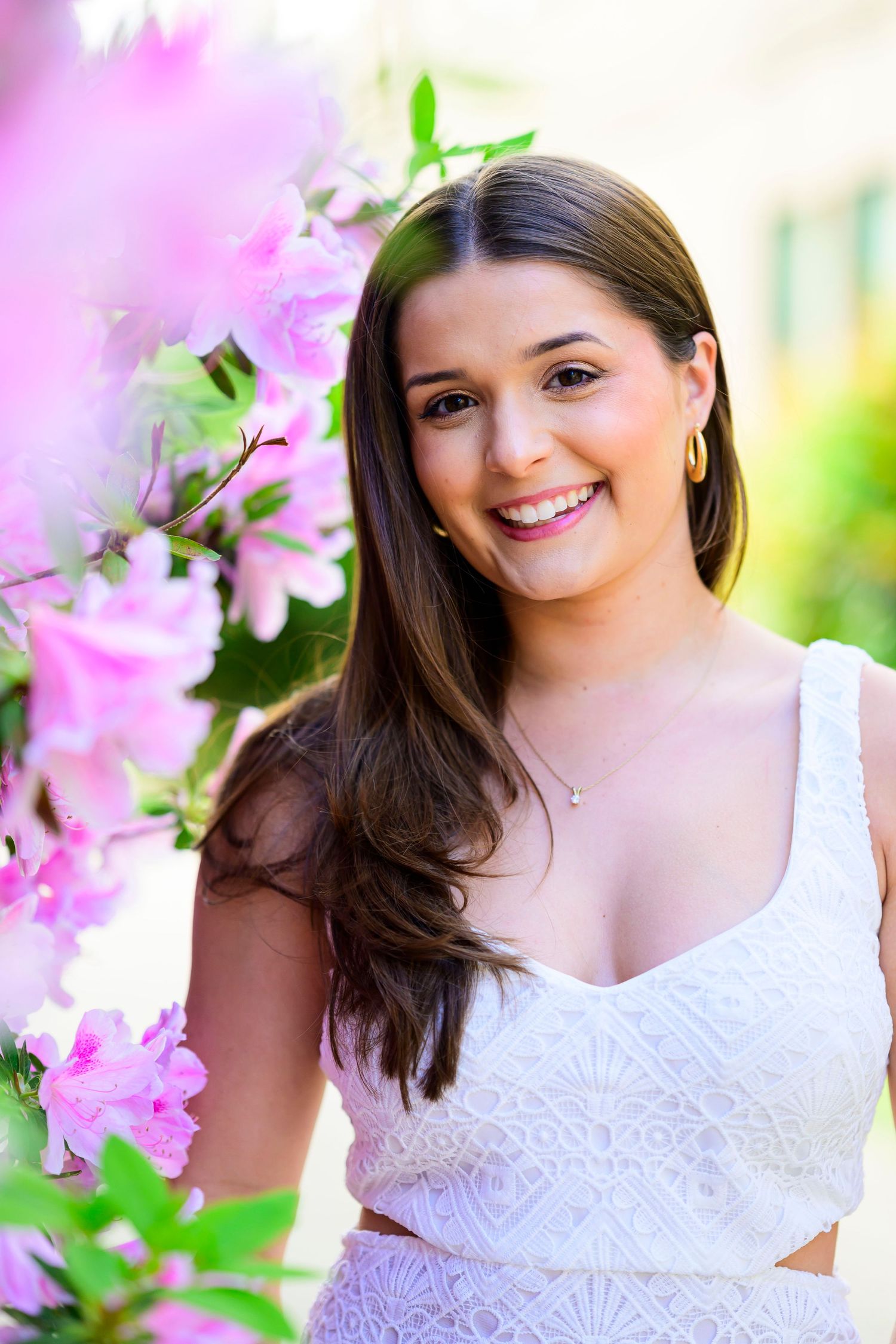 Young woman poses near pink flowers in white dress during spring portrait session.