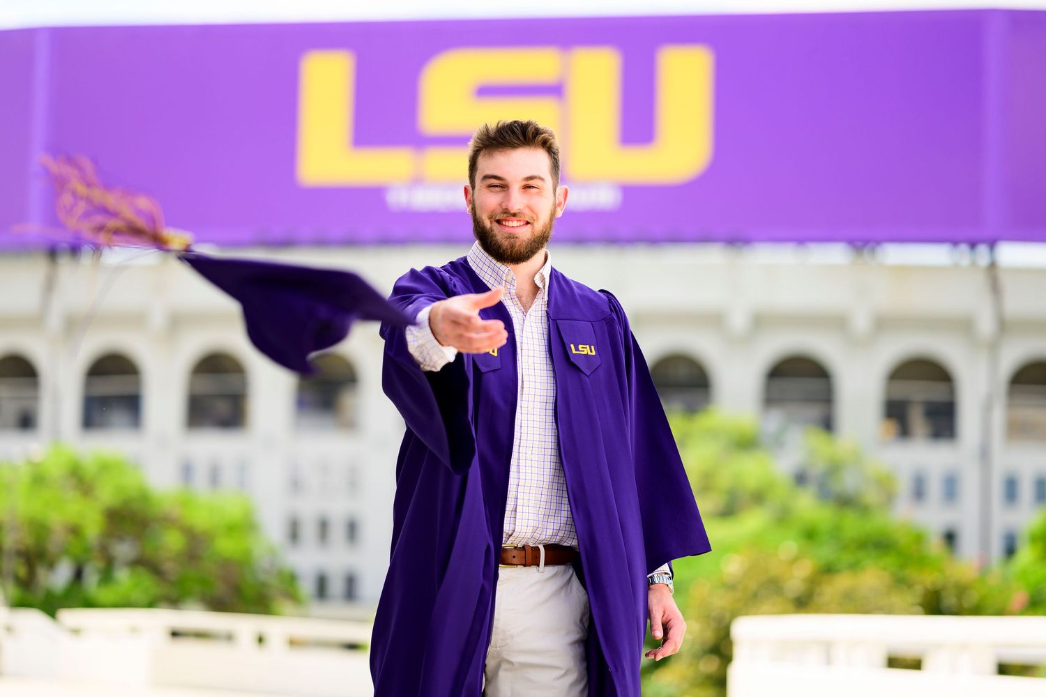 Graduate in purple LSU graduation gown poses in front of university stadium sign.