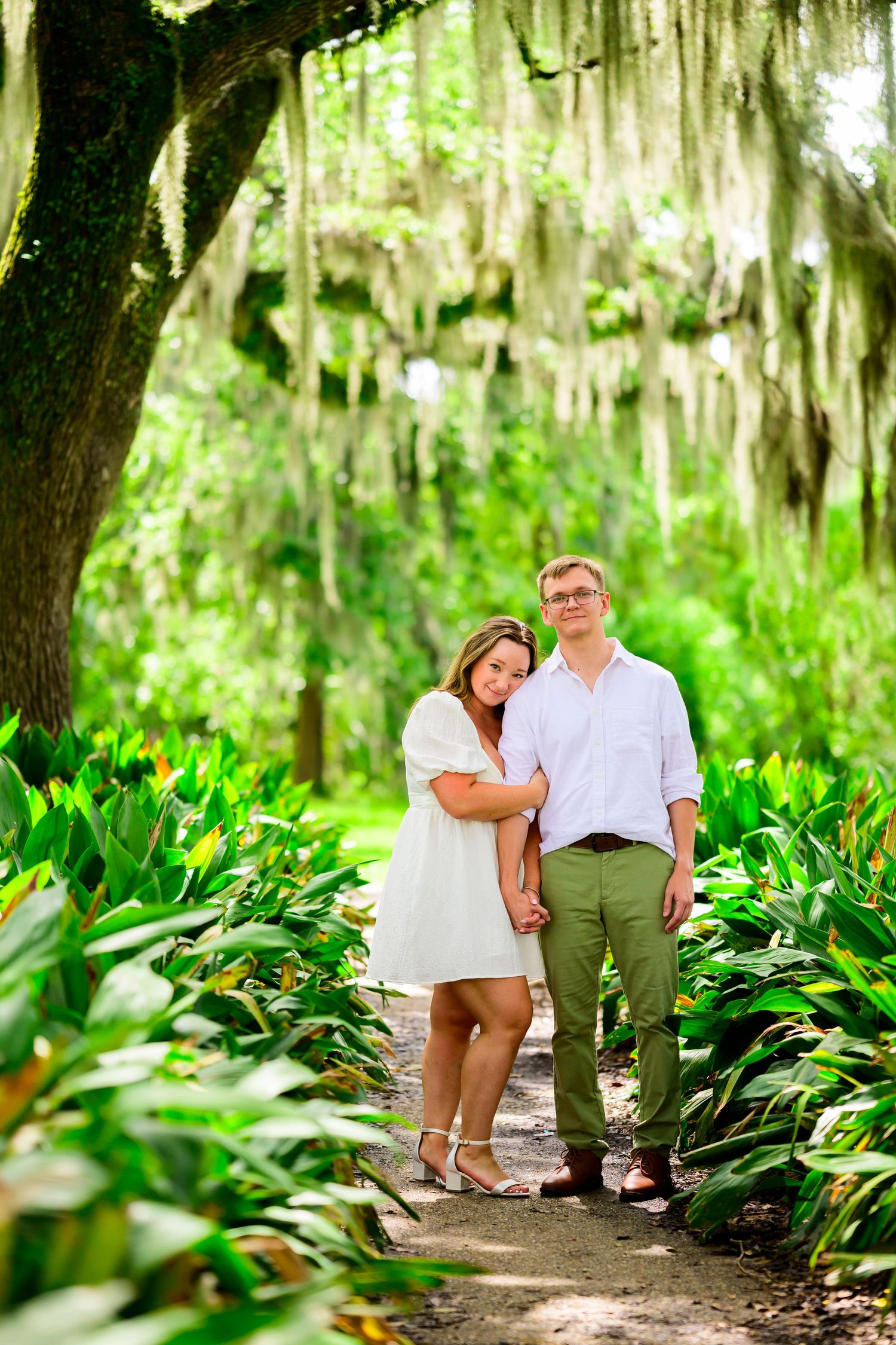 Couple poses together on a tropical garden path under Spanish moss draped trees.