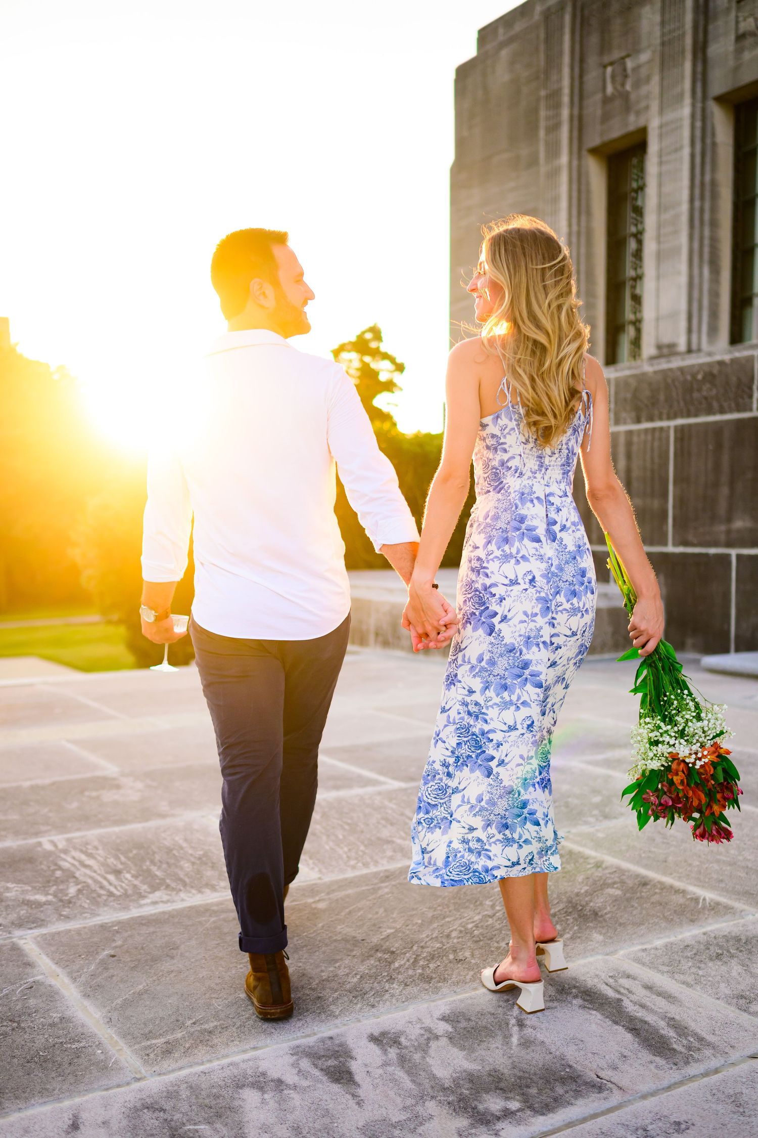 Couple walking hand in hand during golden hour sunset on campus grounds.