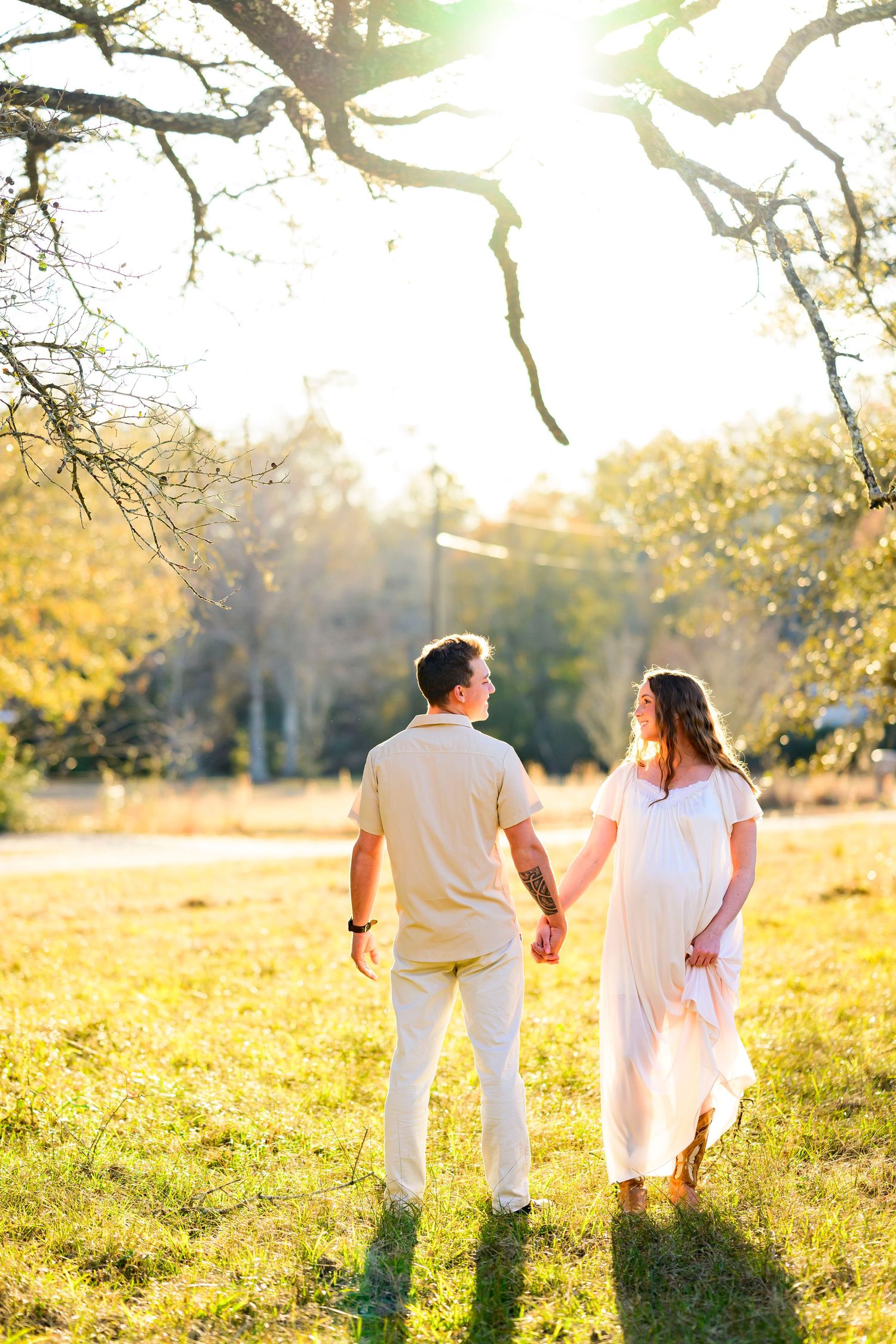 Couple holding hands while walking through a sunny meadow at golden hour.