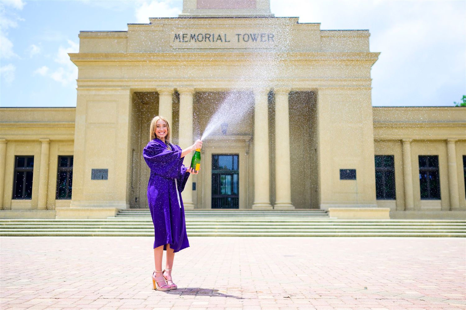 Graduate in purple robe celebrates in front of Memorial Tower on LSU campus.