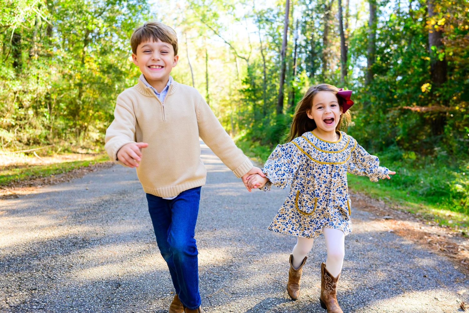 Two children holding hands while running together on a sunlit forest path.