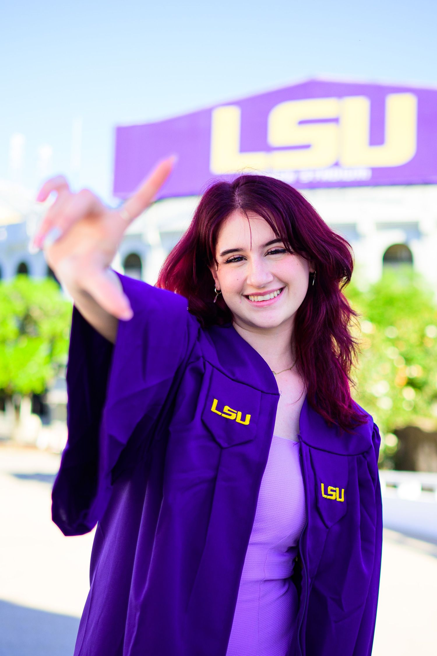 Graduate in purple LSU jacket making peace sign in front of purple university sign.