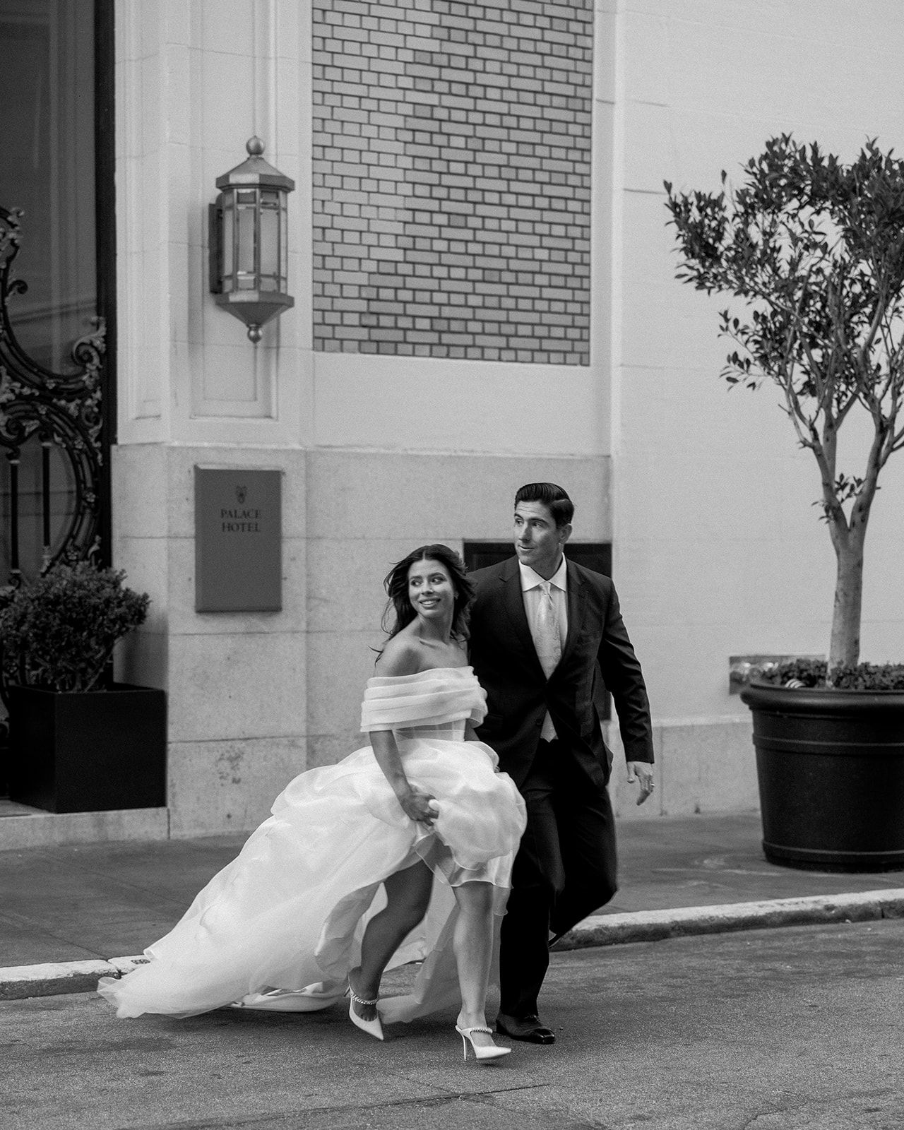 Black and white wedding photo of couple walking outside brick building with lantern.