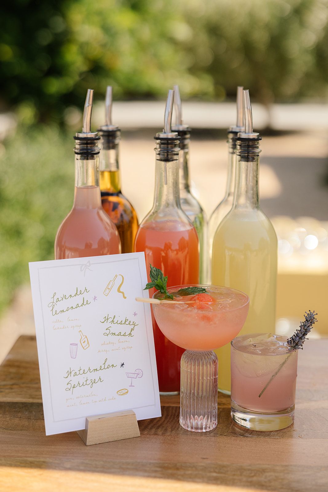 Signature cocktail menu with garnished drinks in glass bottles on wooden table.