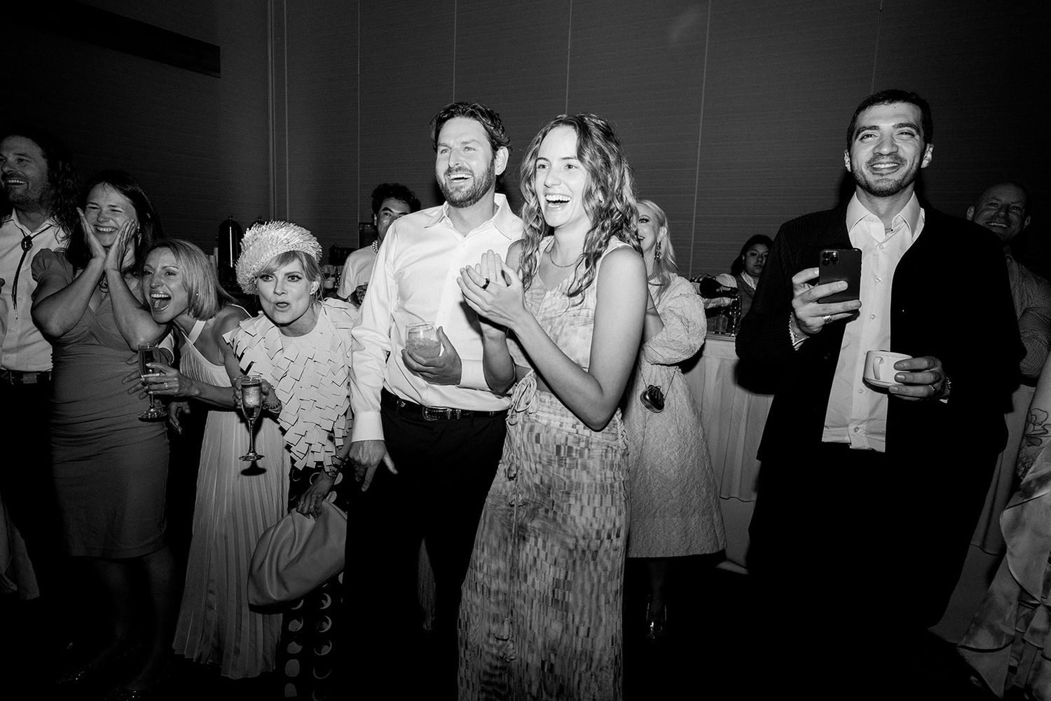 Black and white photo of wedding guests joyfully celebrating on the dance floor at a reception party.