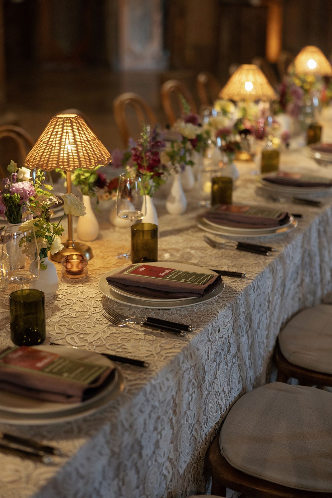 Elegant candlelit dining table with lace tablecloth, floral arrangements, and place settings for a formal event.