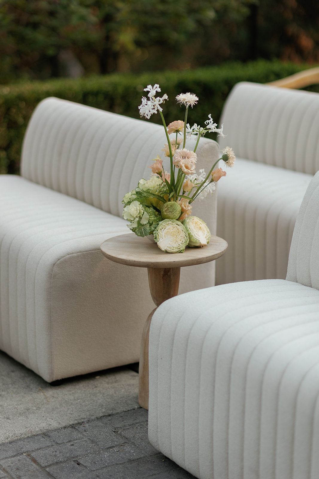 Elegant white ribbed outdoor sofas with a wooden side table holding a soft floral arrangement in pastel tones.