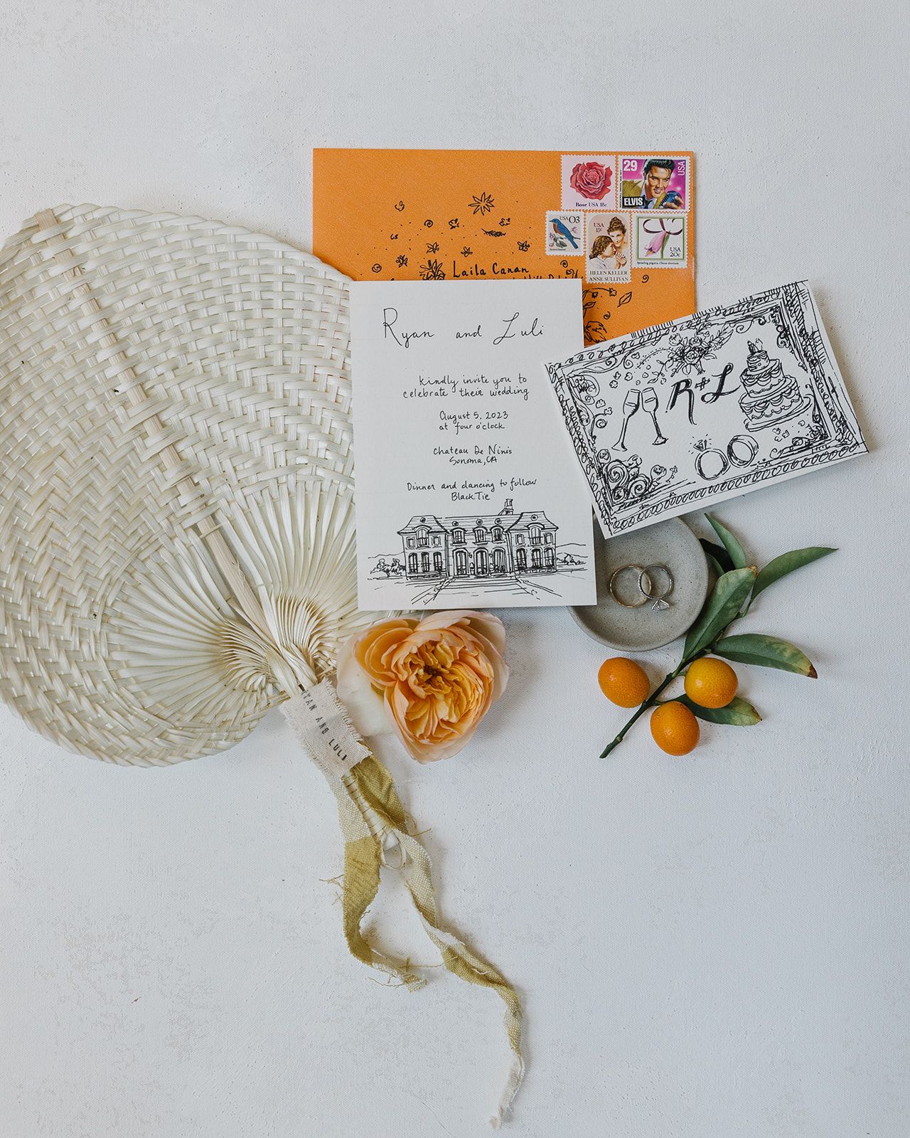 Wedding invitation flatlay with citrus, macrame, and vintage postage stamps.