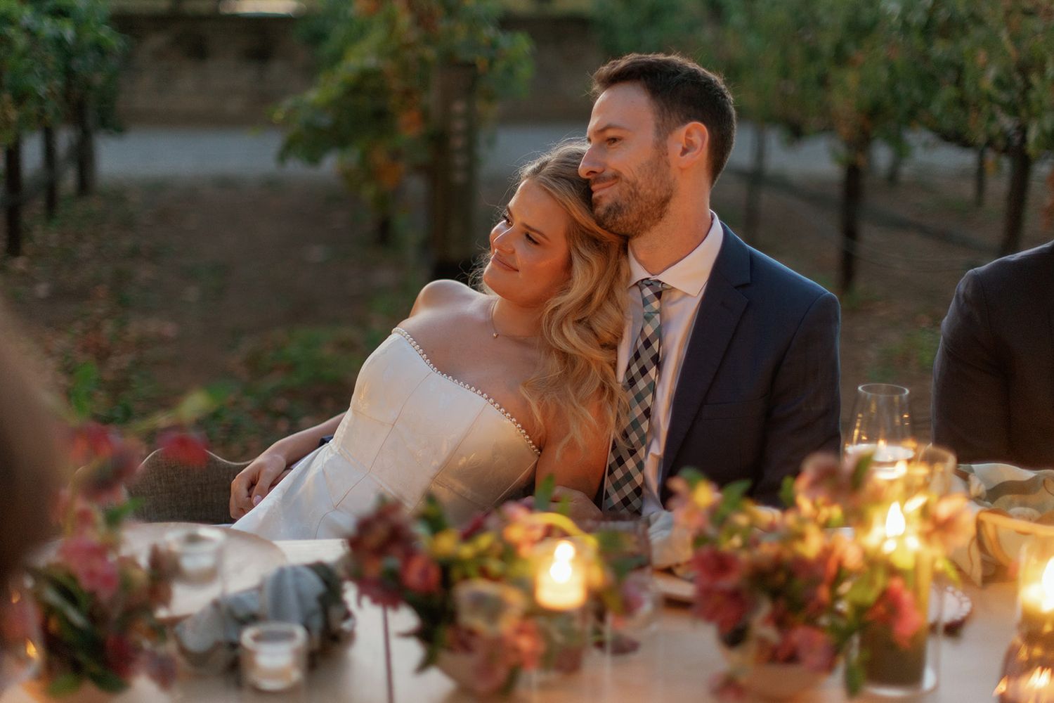 Bride and groom share a tender moment at their romantic outdoor wedding reception table adorned with candles and autumn florals.