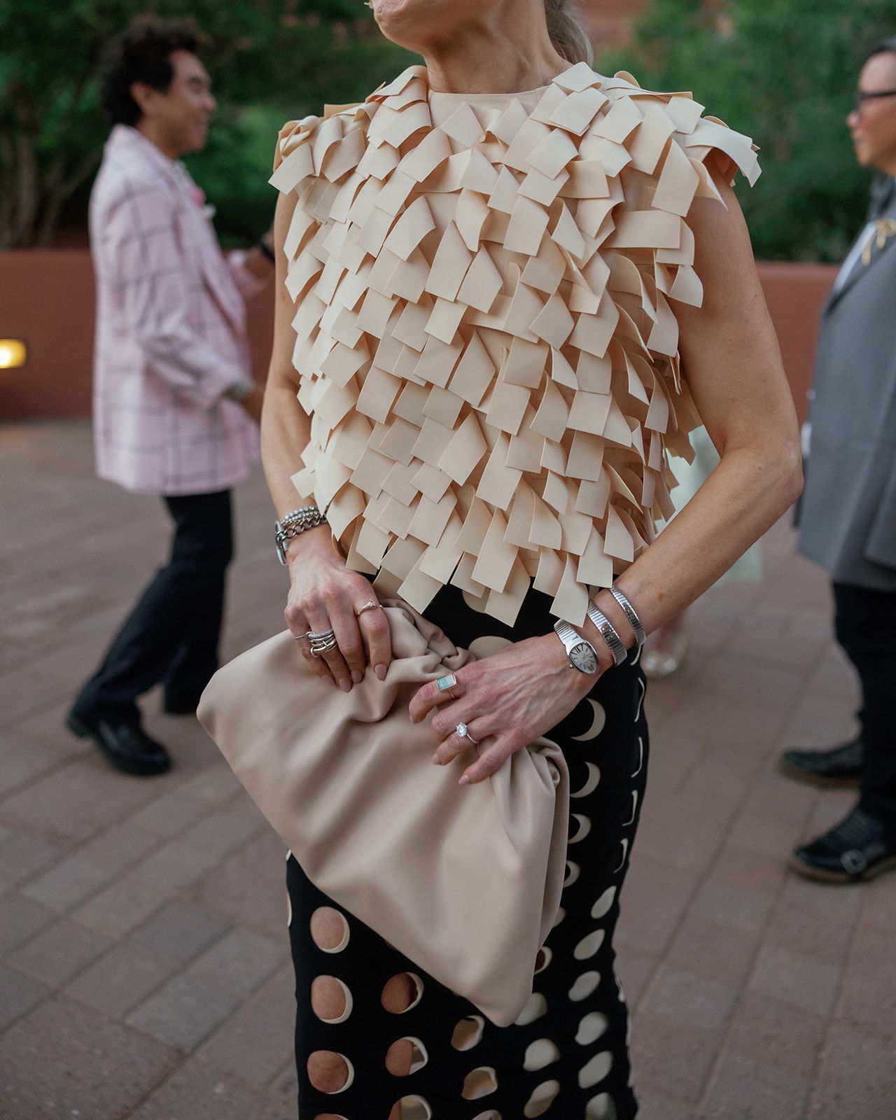 Fashionable outfit featuring cream ruffled sleeveless top, polka dot skirt and beige clutch handbag at evening event.