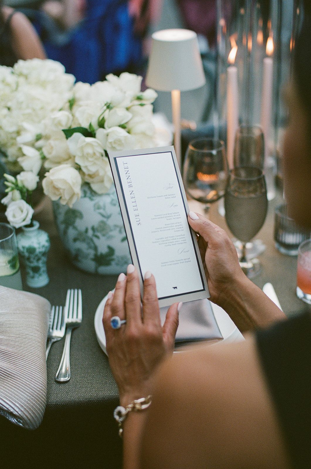 Guest reading menu at elegant dinner table with white roses and candlelight during formal event.