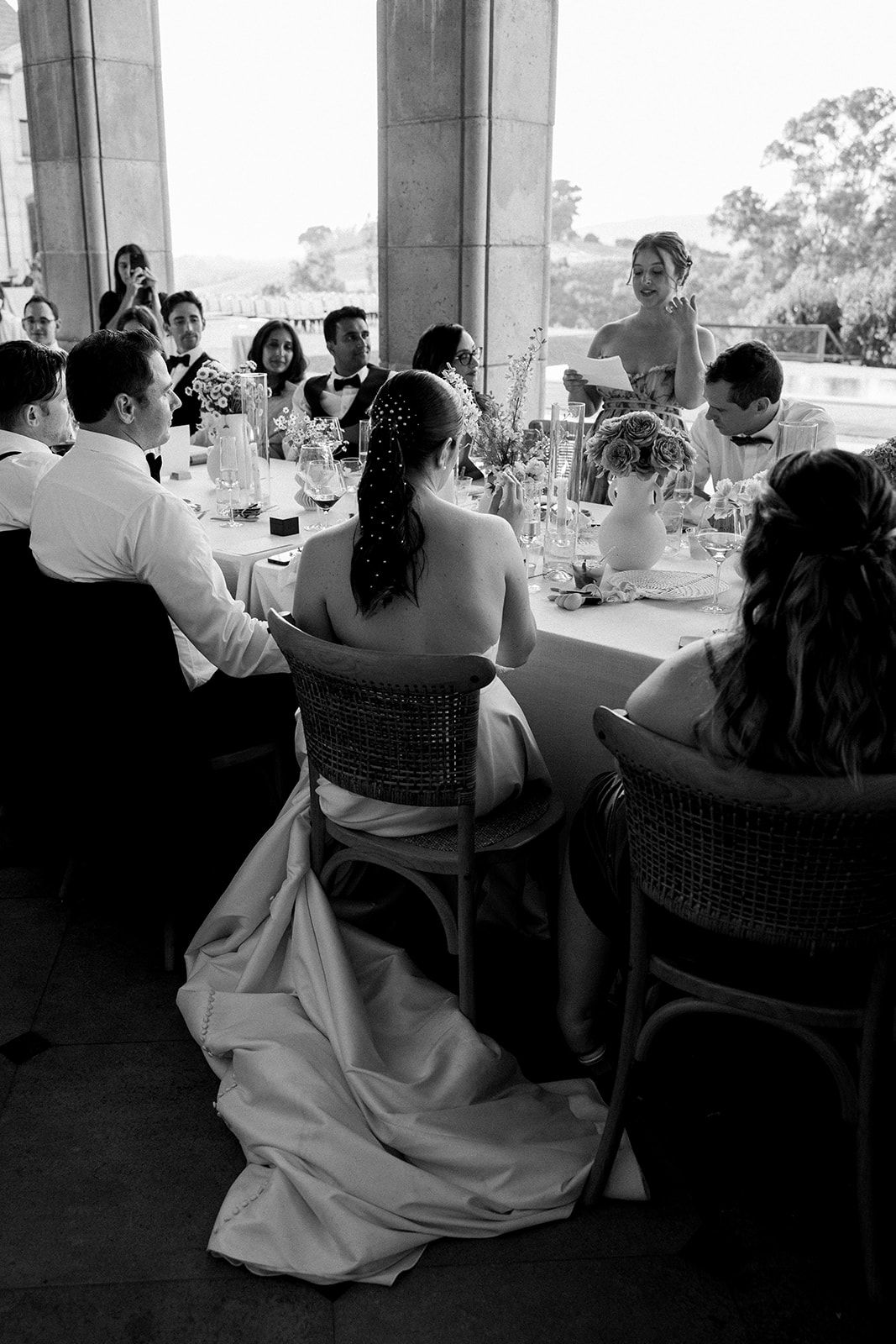 Black and white photo of wedding reception guests seated at outdoor dining table.