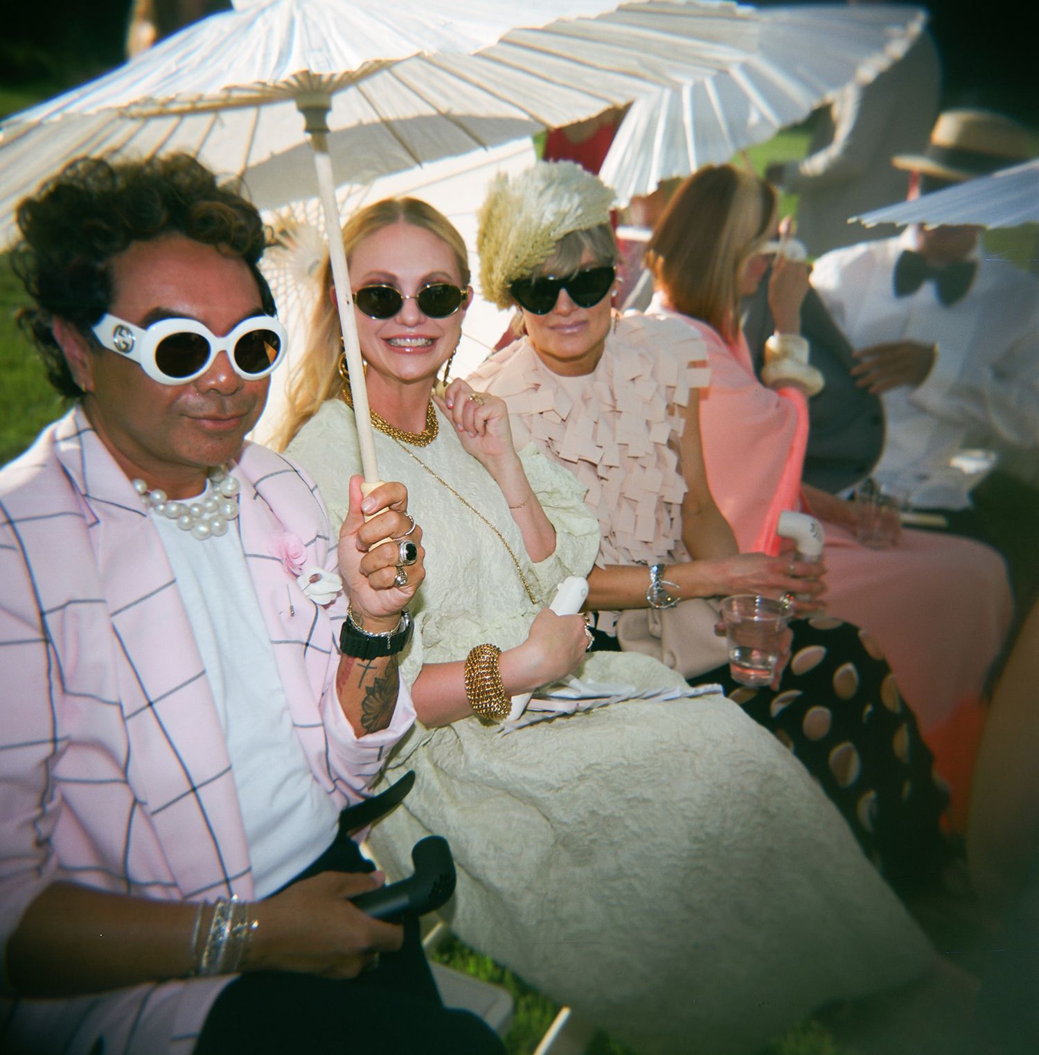 A group of friends enjoying a sunny outdoor party with parasols and retro sunglasses in vintage-style photography.