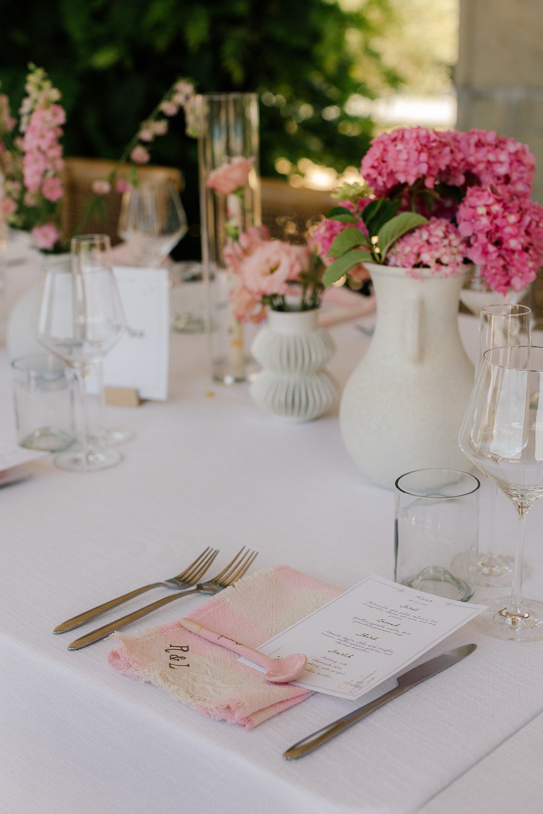 Elegant table setting with pink floral centerpieces, glassware and menu cards.