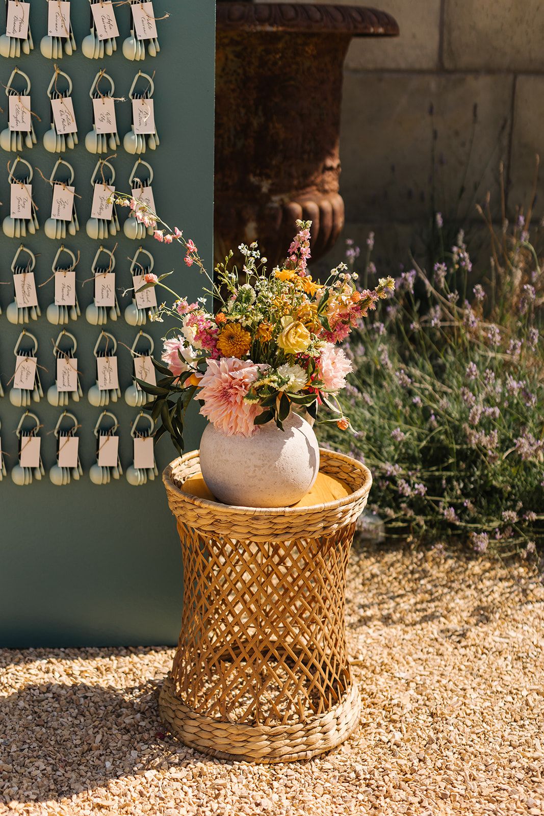 Floral centerpiece on woven rattan stand next to wall display of place cards.