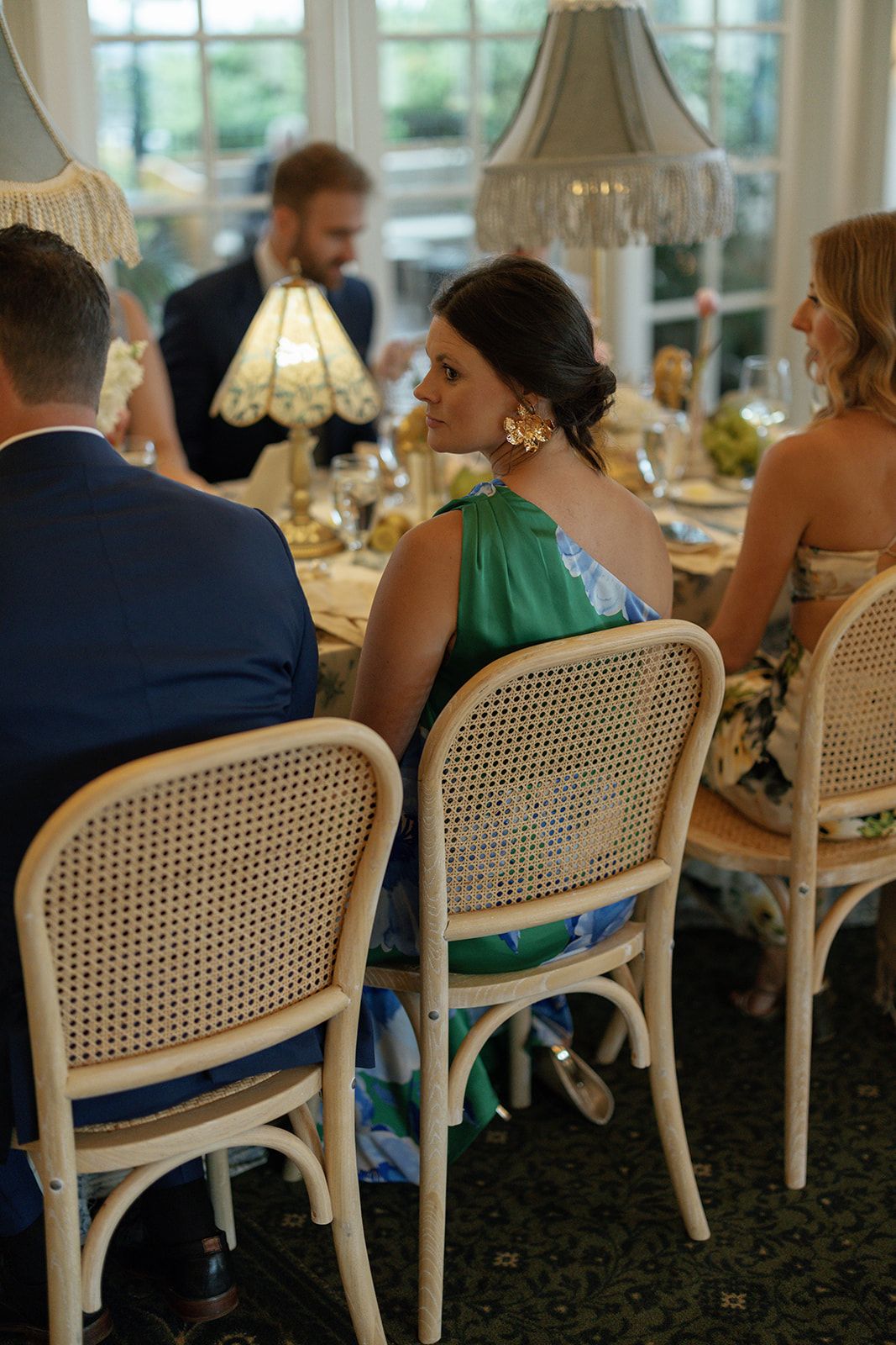 Elegant dinner party setting with white cane-back dining chairs and glowing table lamps in a formal dining room.