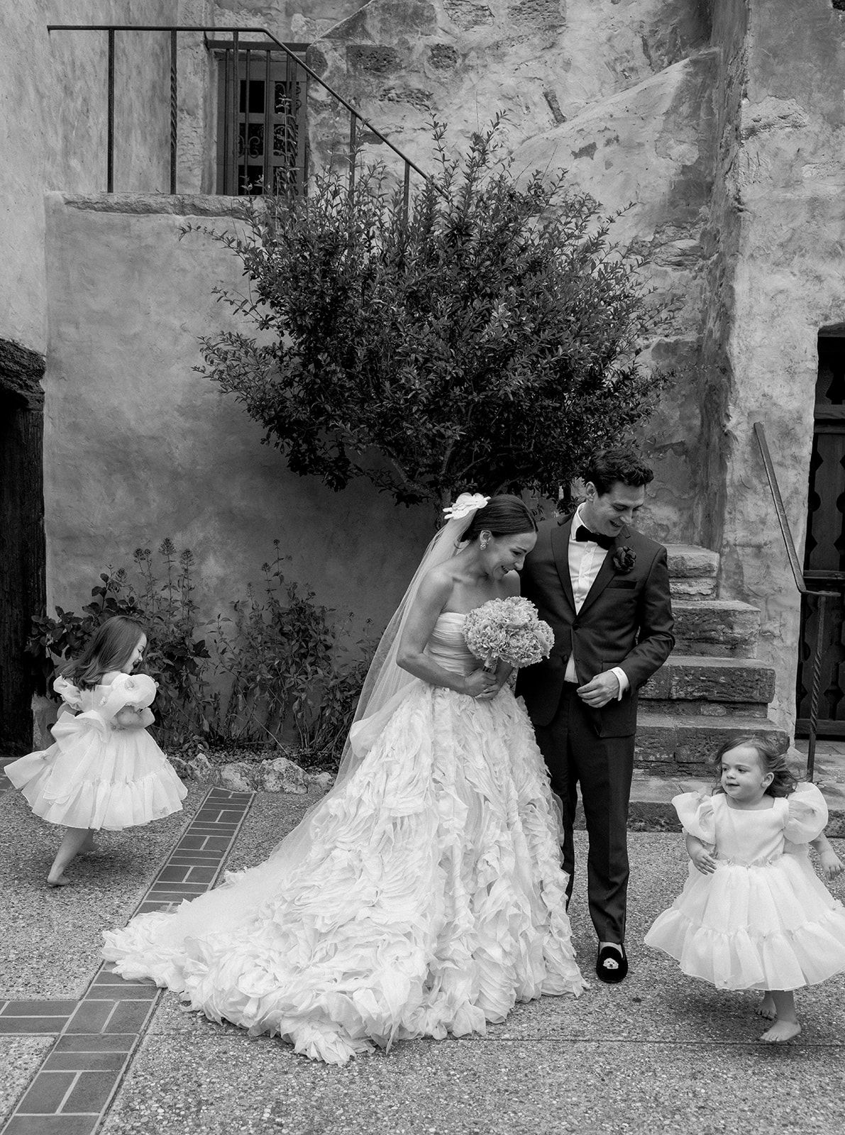 A vintage black and white wedding photo showing a couple in formal attire with two small children in white dresses.