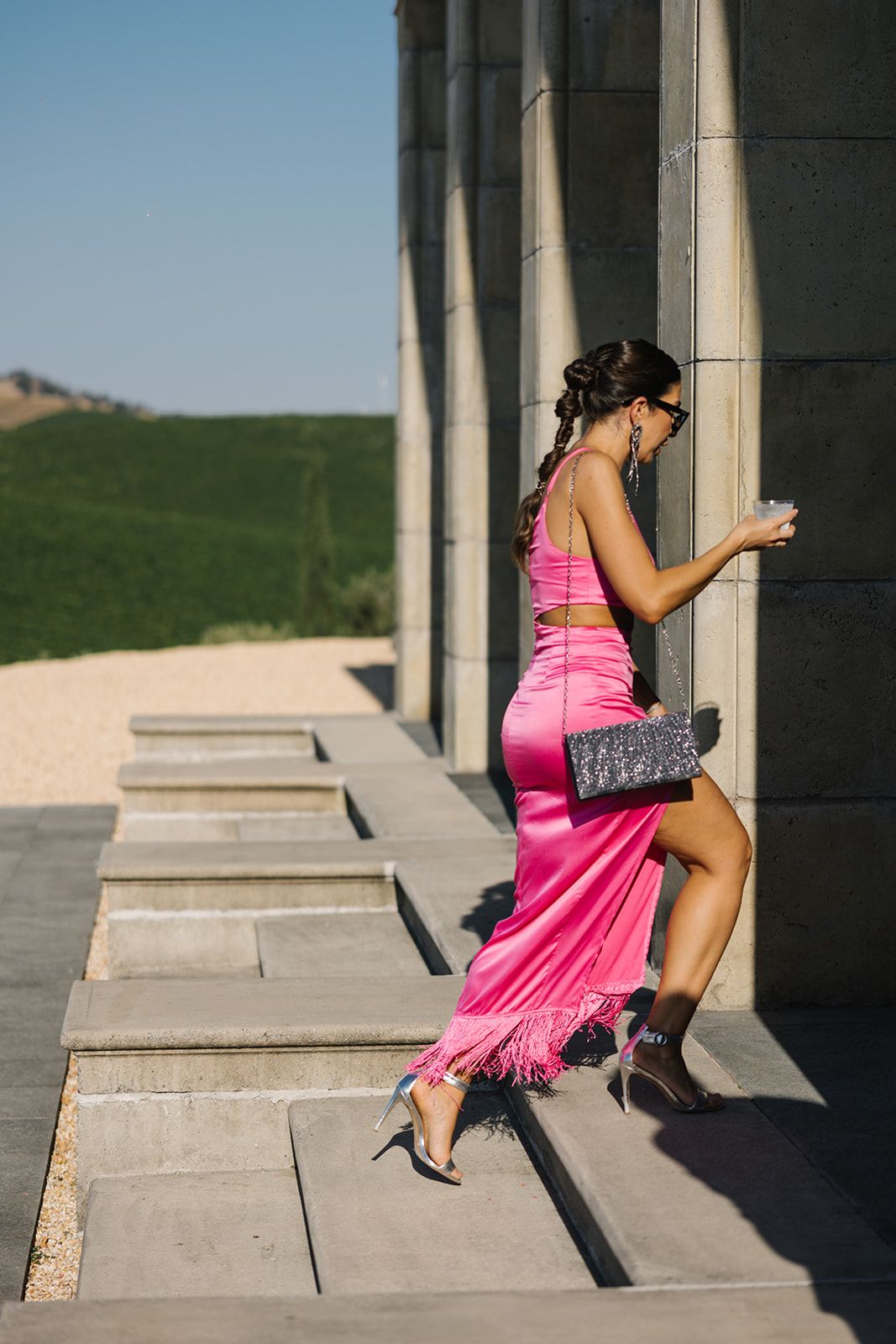 Woman in vibrant pink dress posing on stone steps against architectural columns.