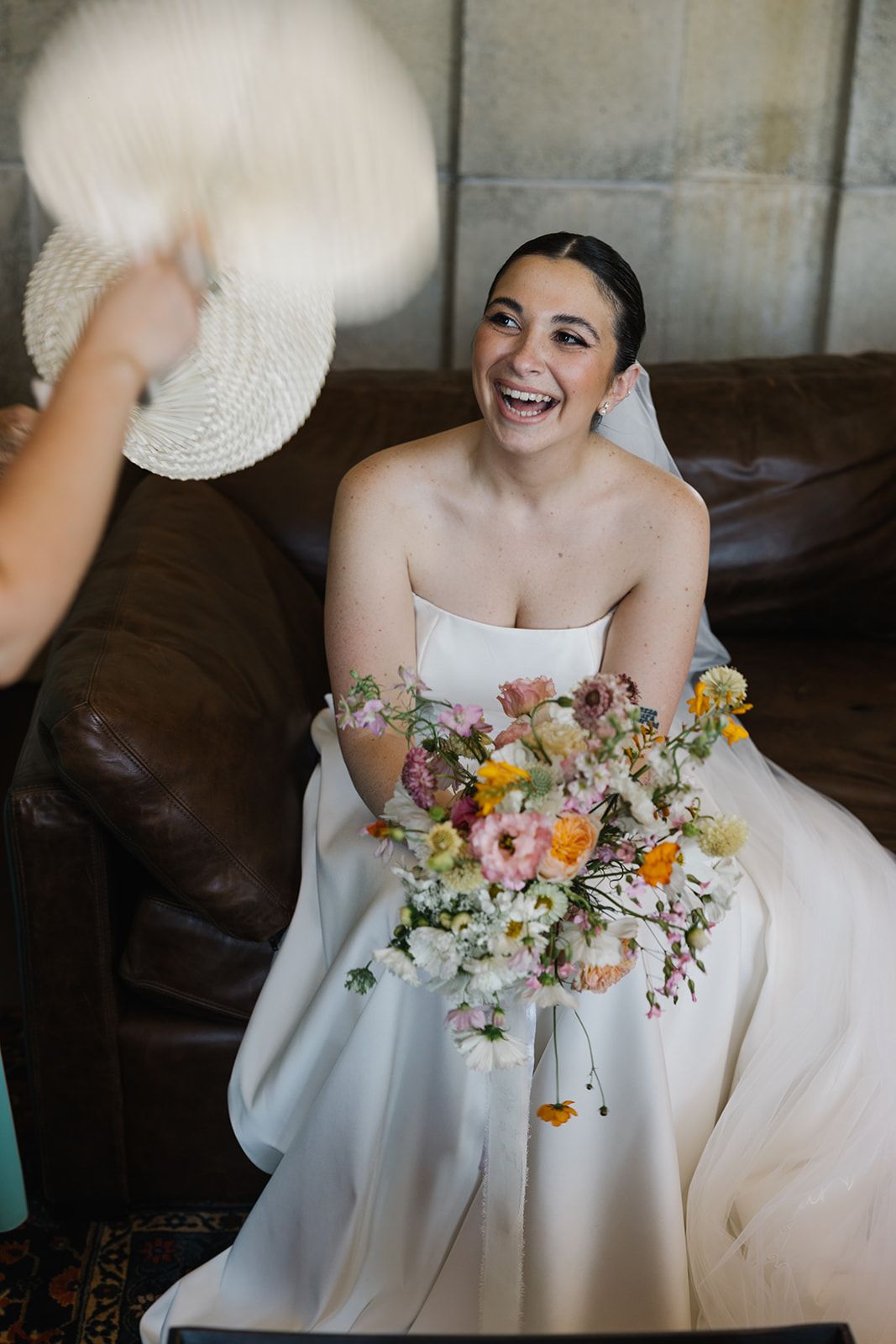 Candid moment of joyful laughter during wedding preparations with vibrant floral bouquet.