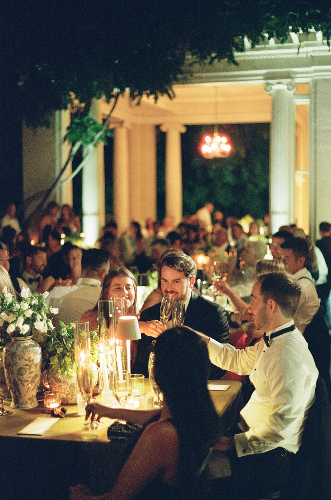 Candlelit wedding reception dinner with guests seated at elegant tables in an illuminated outdoor venue at night.