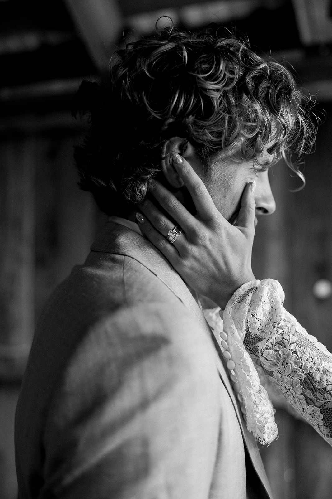 Black and white photo of a bride in lace glove tenderly touching grooms face at wedding ceremony.