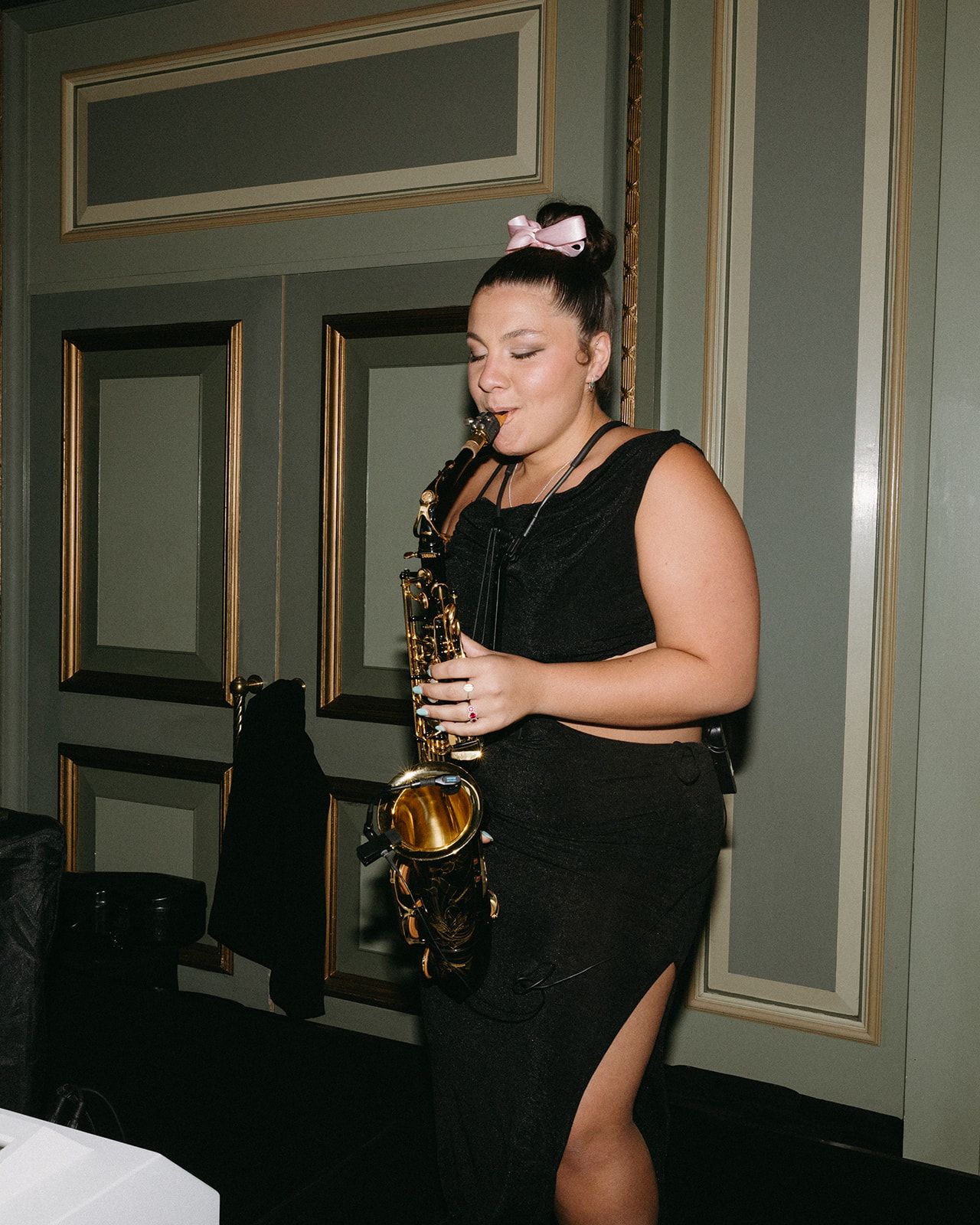 Musician performing on saxophone in an ornate venue with decorative molding.
