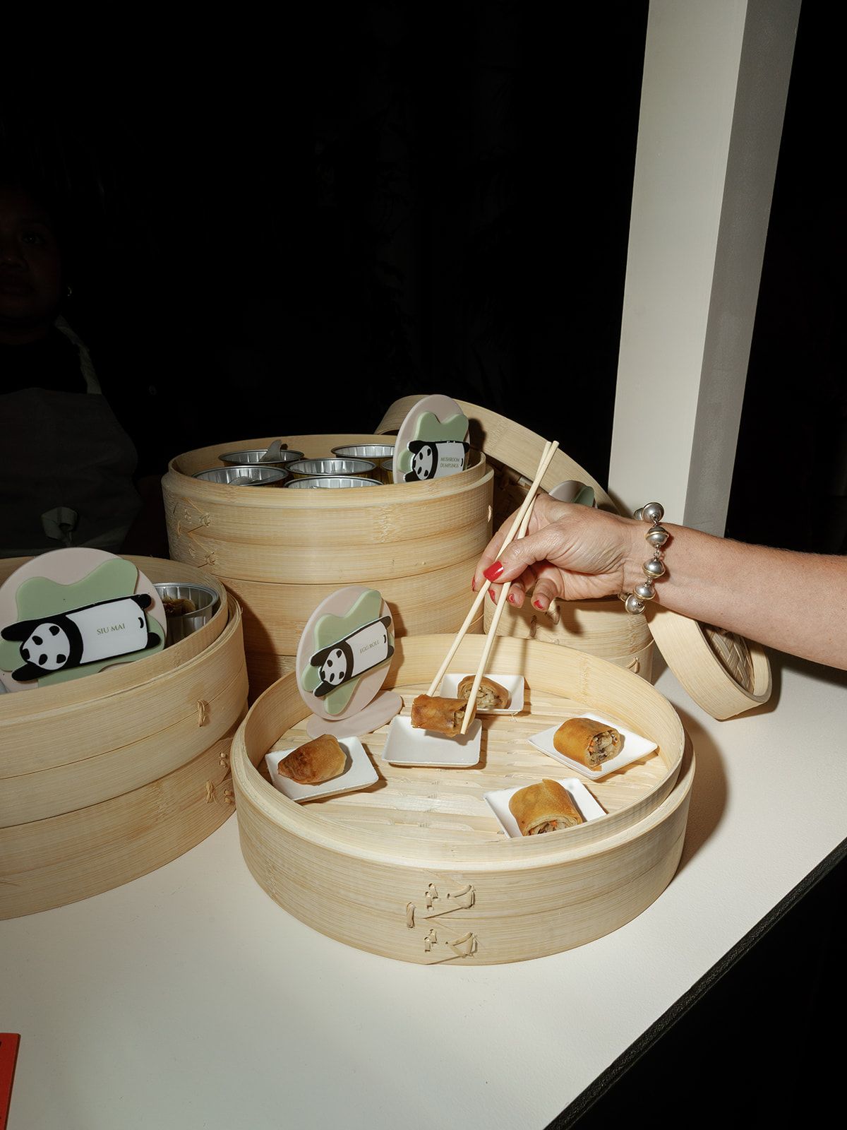 Hand using chopsticks to pick up dim sum cookies from bamboo steamer baskets at an Asian-themed event.