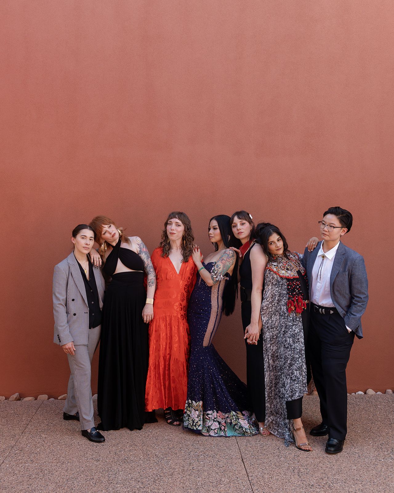 A group of friends in formal attire pose together against a terracotta colored wall for a special occasion.