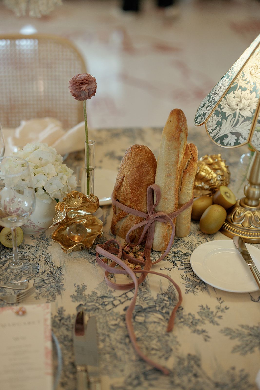 Small decorative dining table scene with rustic bread, olives, and silver dining accessories on a floral patterned tablecloth.