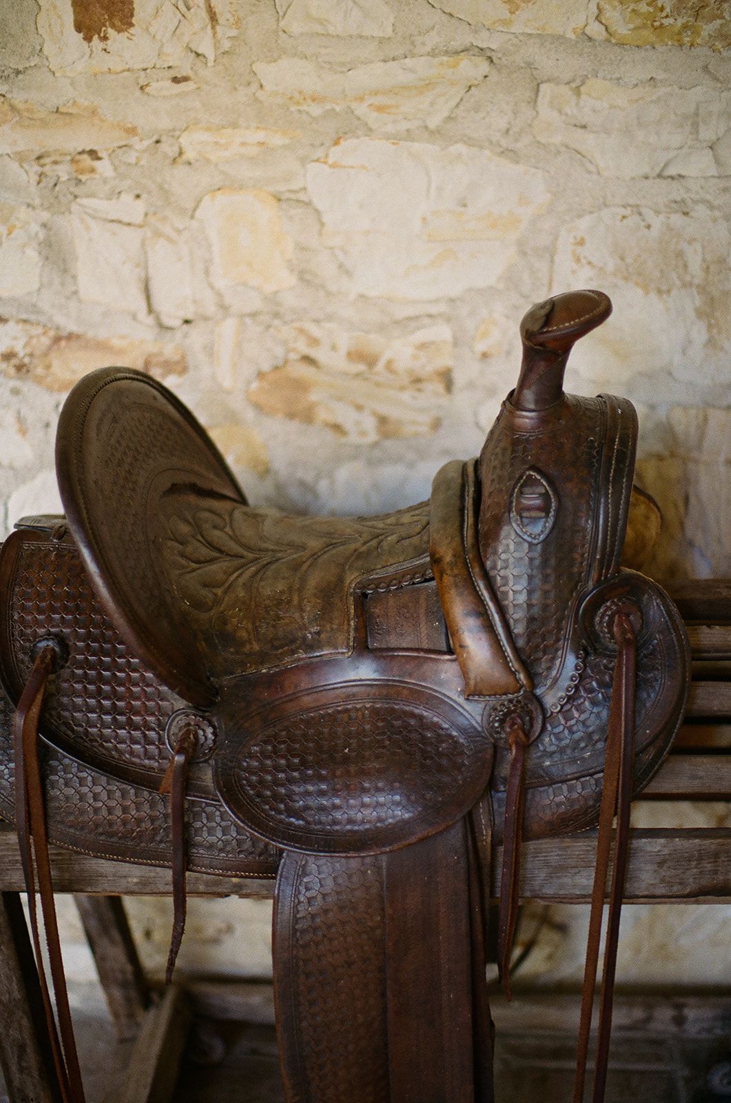 Row of vintage brown leather western saddles displayed against a rustic stone wall.