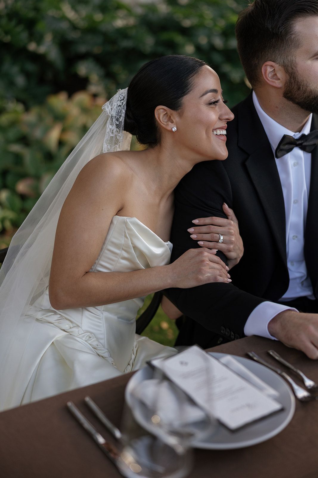 A sequence of candid wedding photos showing tender moments between a couple seated at a dining table.