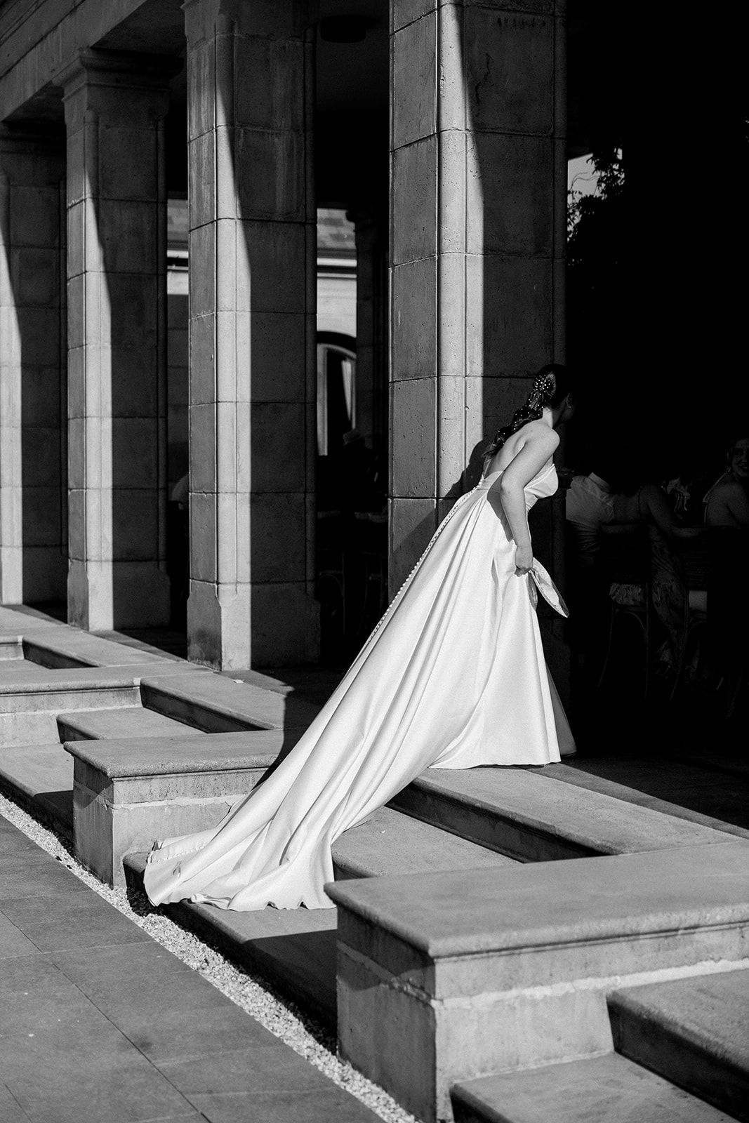 Dramatic black and white photo of bride in flowing wedding gown ascending stone steps.