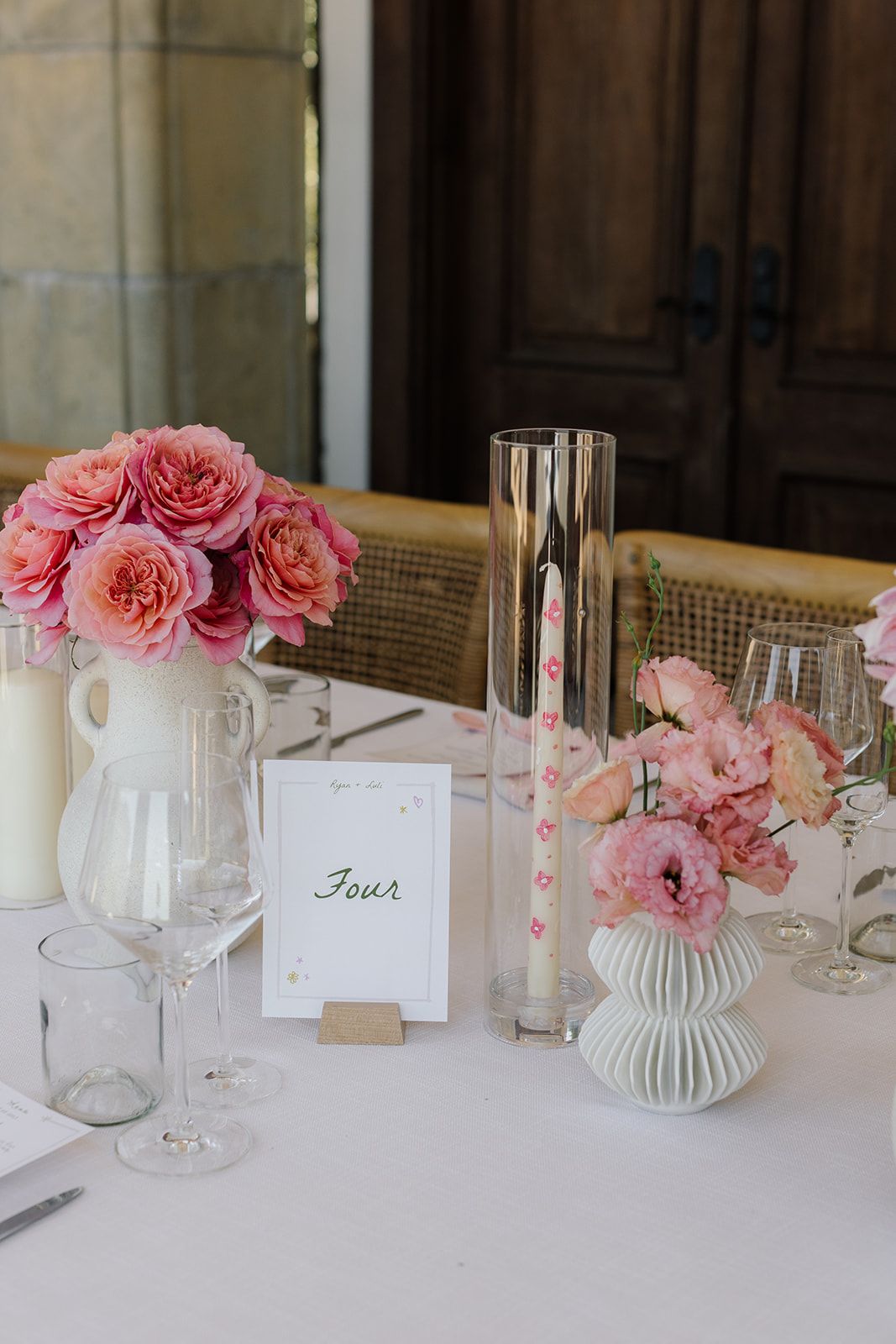 Wedding table decor with pink roses, ribbed vases, and table number card.