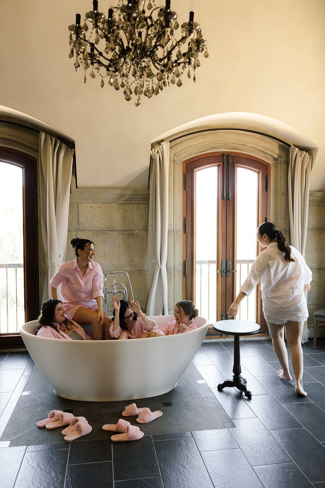 Group getting ready in luxury bathroom with ornate chandelier and freestanding tub.