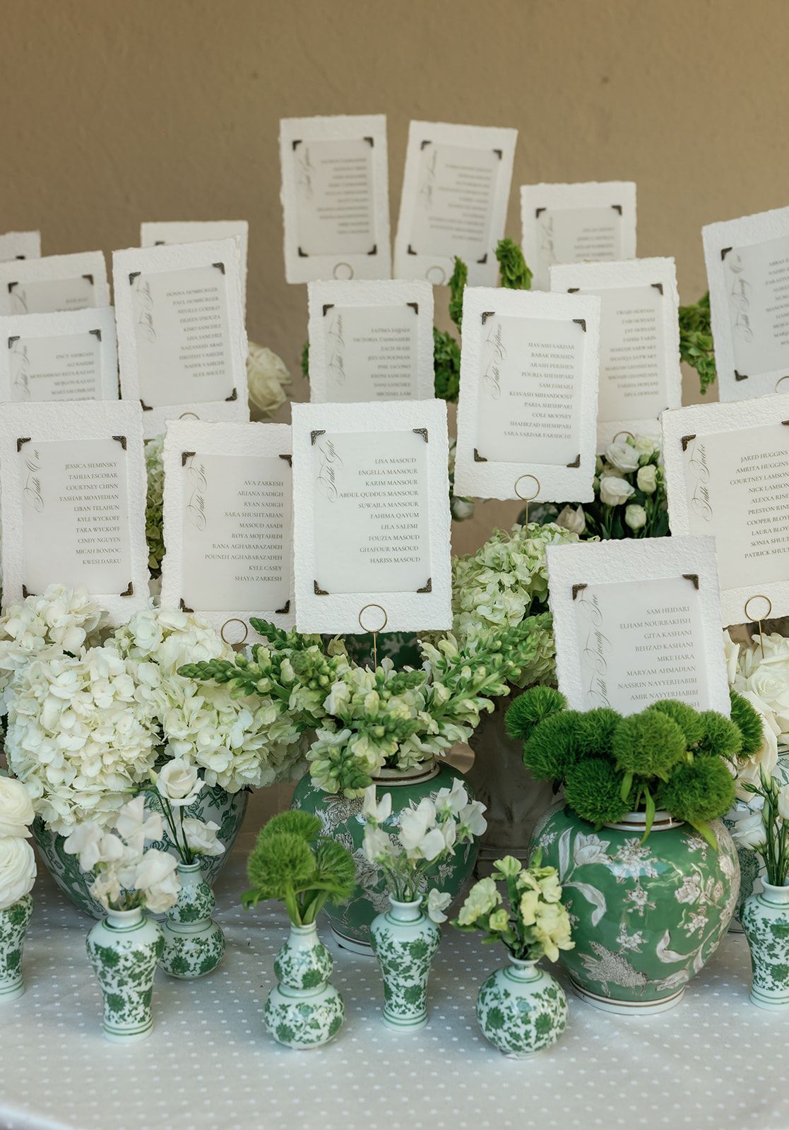 A row of white wedding escort cards displayed above elegant white hydrangea and greenery floral arrangements in glass vases.